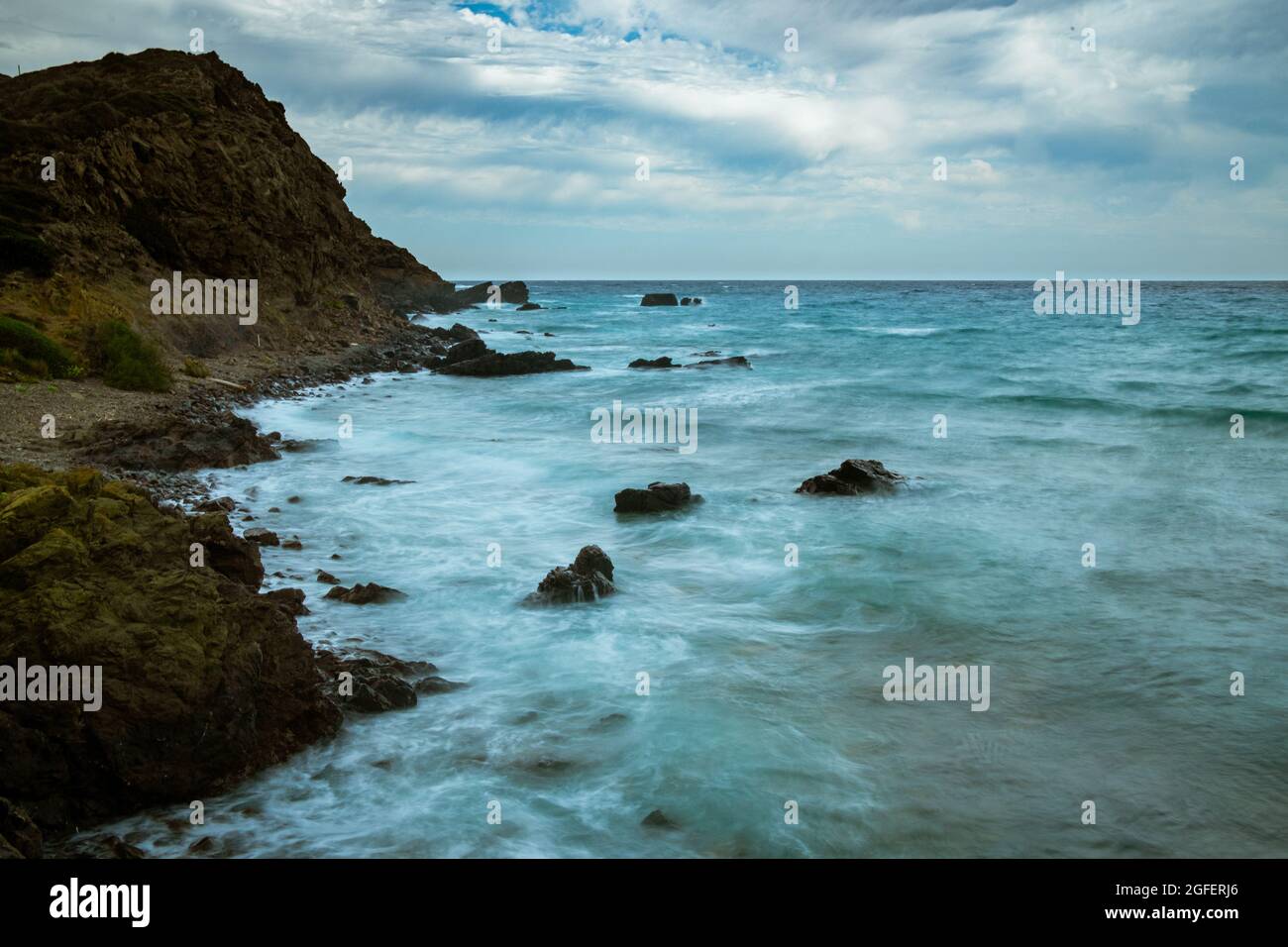 Felsige Strandlandschaft bei Sturm mit bewölktem Himmel. Dramatische, lange Exposition von Meereswellen, die auf Felsen brechen. Stockfoto