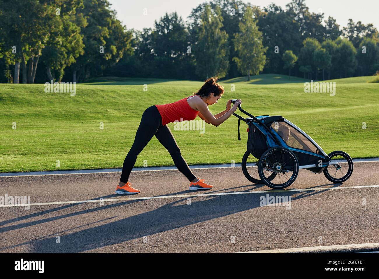 Sportliche Frau, während die Mutterschaft mit ihrem Sohn im Kinderwagen im Stadtpark Fitness und Training macht. Teil einer Reihe von Übungen für junge Frauen mit Stockfoto