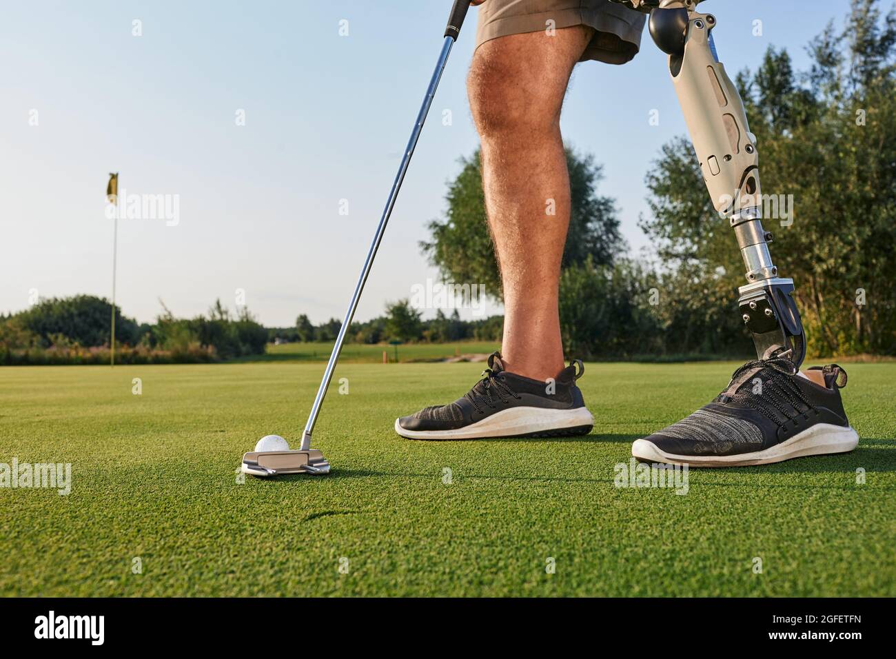 Professioneller Golfspieler mit Beinprothese, der während des Golfspiels mit Putter auf den Golfball trifft. Konzept der Willenskraft von Menschen mit Behinderungen im Sport Stockfoto