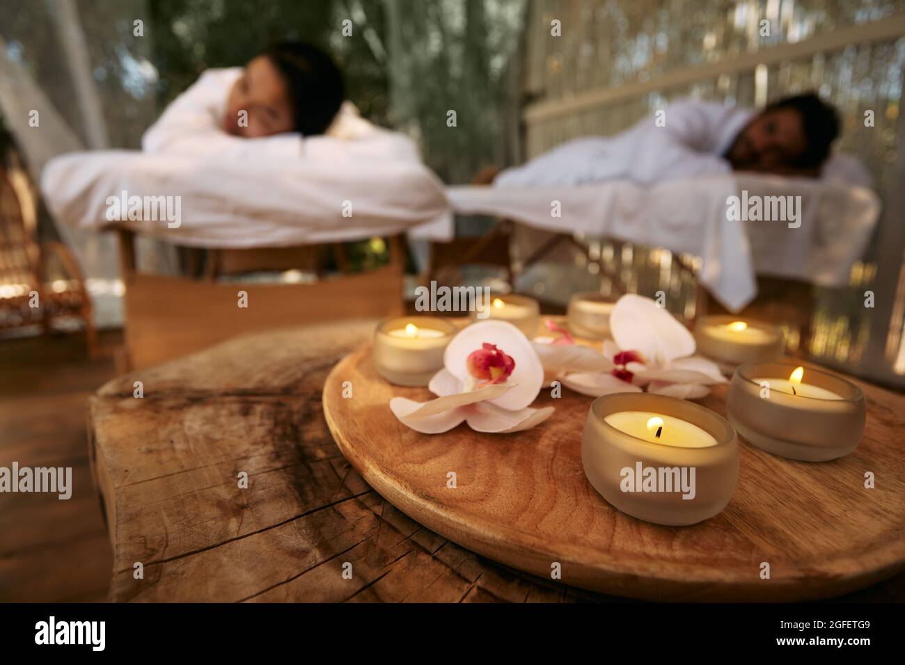 Aromamassage für Paare. Paare liegen während des Tages-Spa und romantischen Wochenendes mit Kerzen und Orchideenblumen im Spa Resort auf Massageliegen Stockfoto