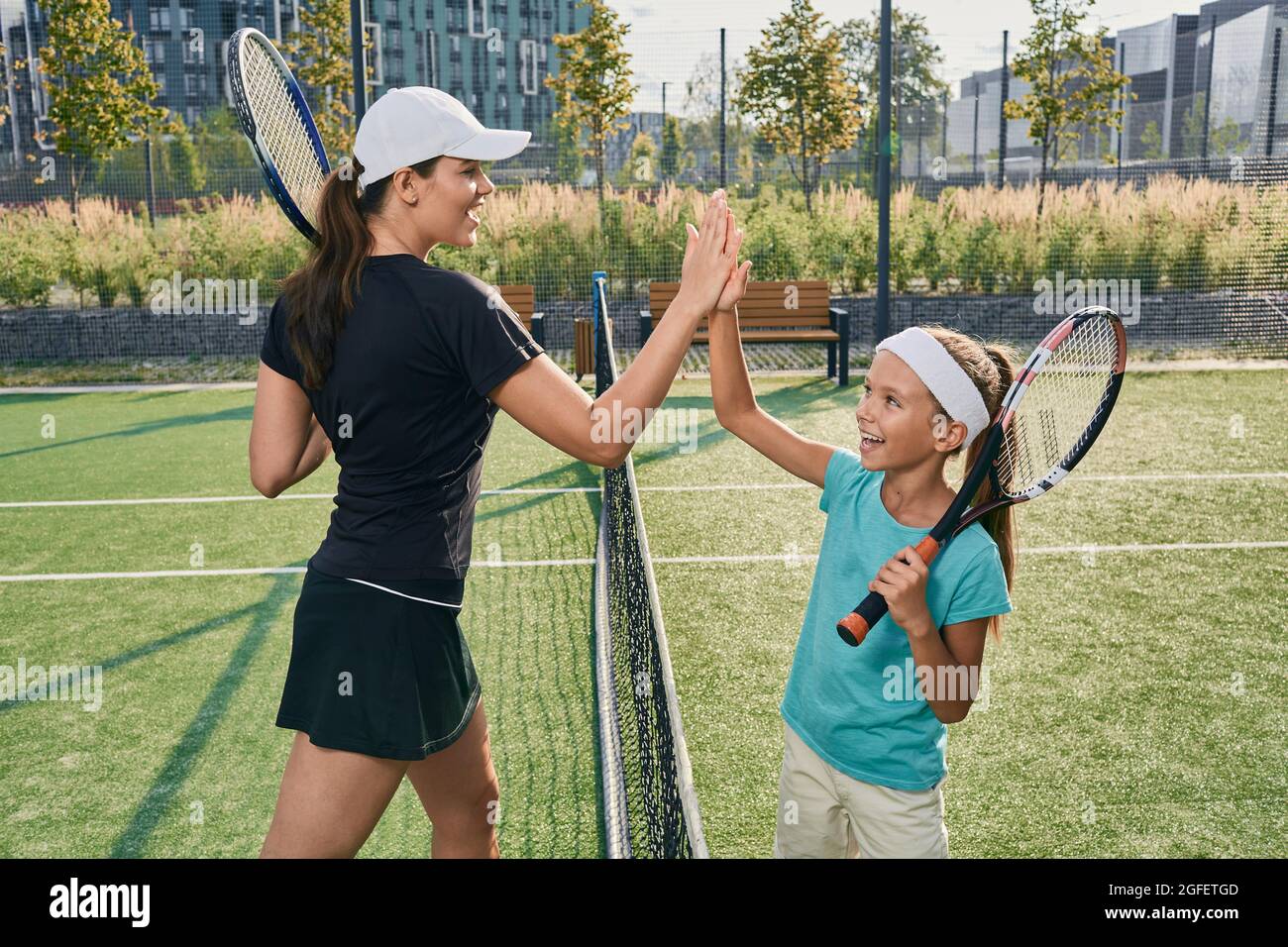 Das Kind gibt ihrem Trainer fünf, nachdem er Tennis gespielt hat. Tennistraining für Kinder auf dem Freiluftplatz Stockfoto