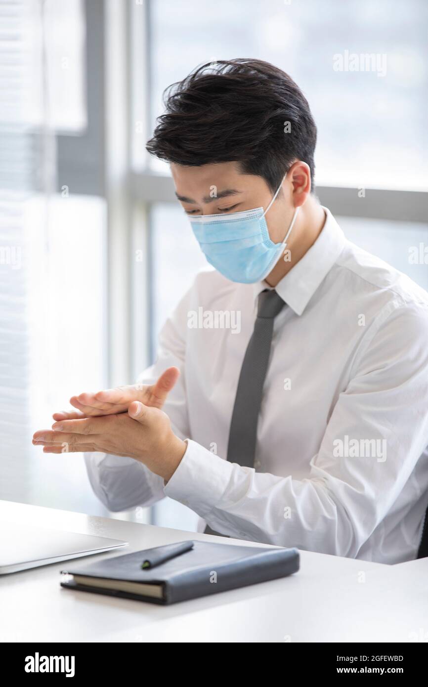 Junger Geschäftsmann, der im Büro Handdesinfektionsmittel verwendet Stockfoto