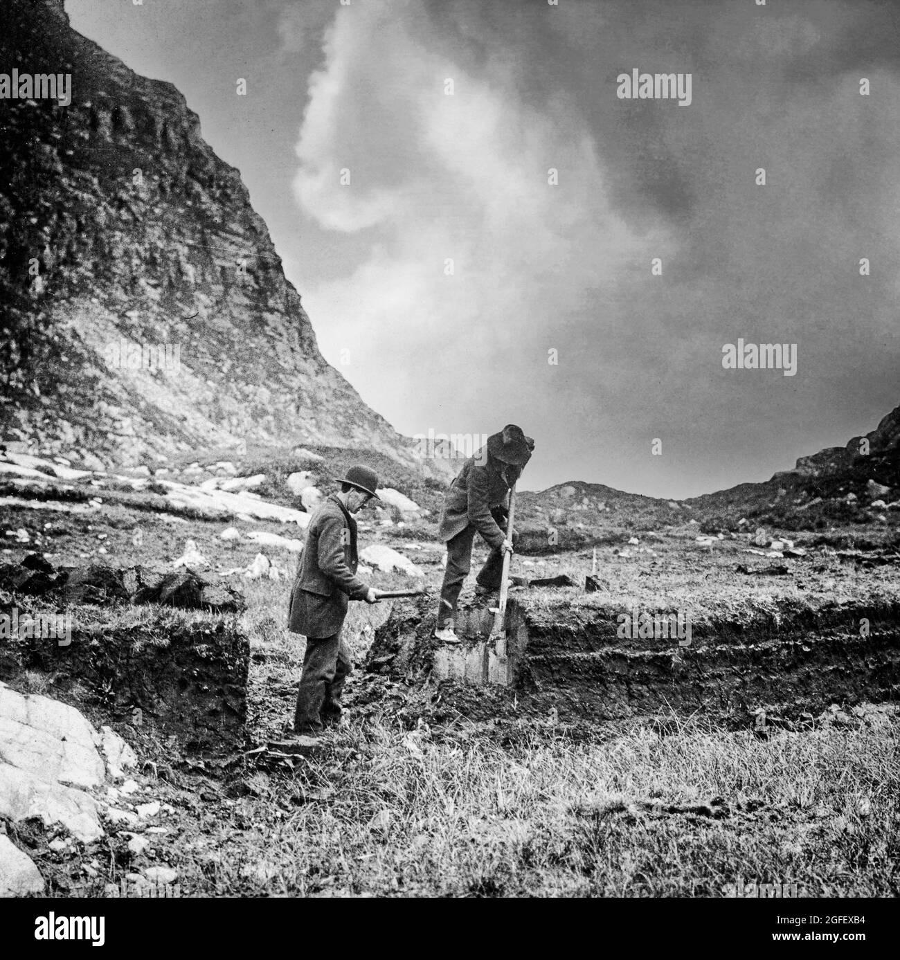 Ein Foto aus dem frühen 20. Jahrhundert, auf dem Einheimische im Gap of Dunloe, einem schmalen Bergpass, der die MacGillycuddy's Reeks Bergkette im Westen von der Purple Mountain Group Range im Osten des Killarney National Park in der Grafschaft Kerry, Irland, trennt, Rasen (auch Torf genannt) ausgraben Stockfoto