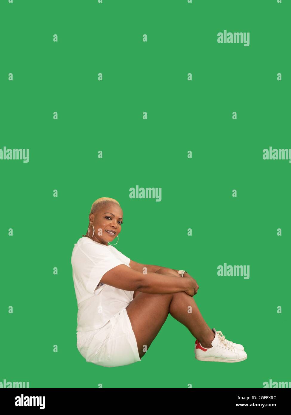 Vertikales Porträt einer lächelnden, schönen Afro-Amerikanerin, die Sportswear-Sitze auf einem grünen Hintergrund trägt Stockfoto