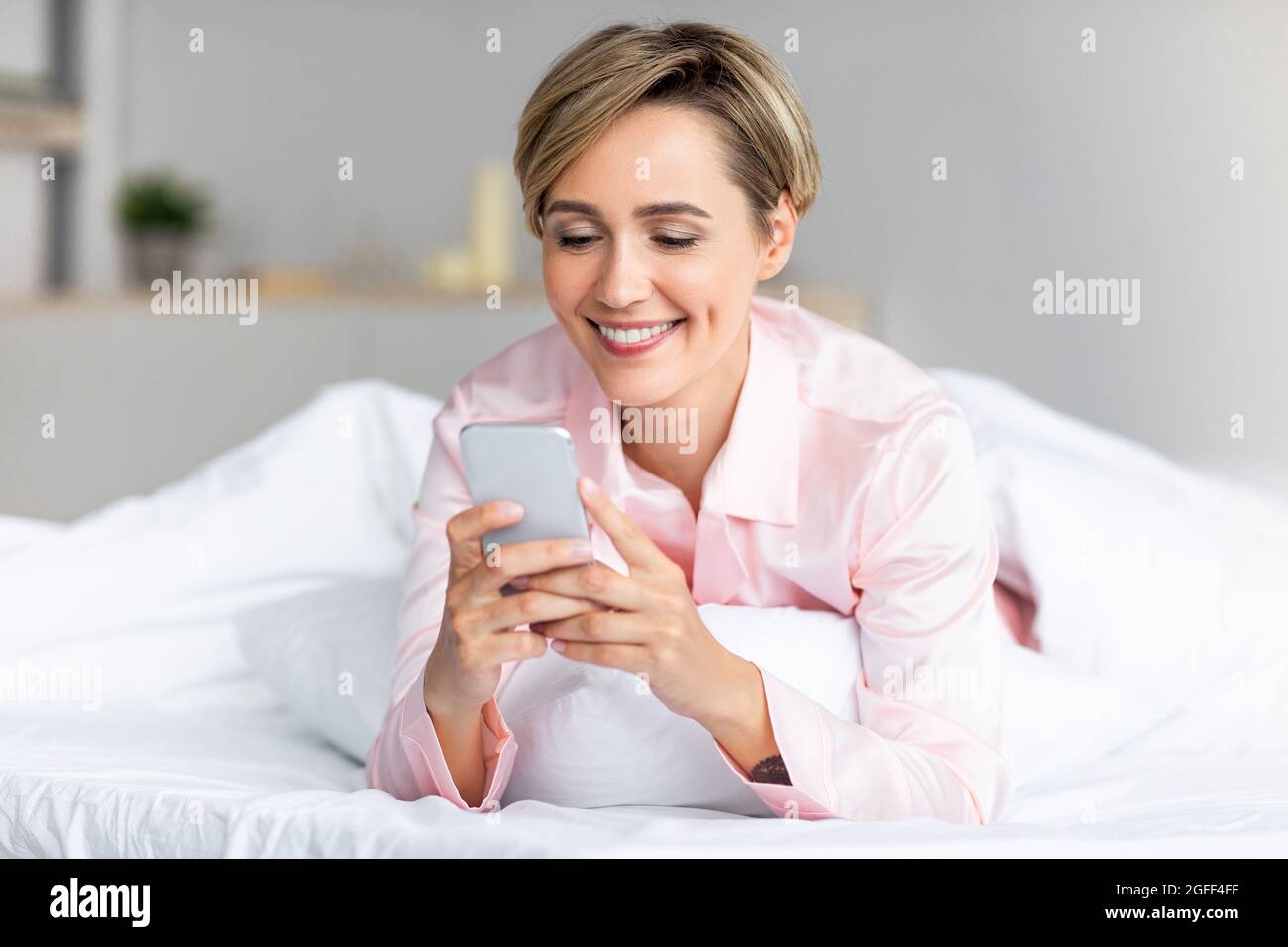 Glückliche Frau, die im Bett lag und SMS am Telefon las Stockfoto