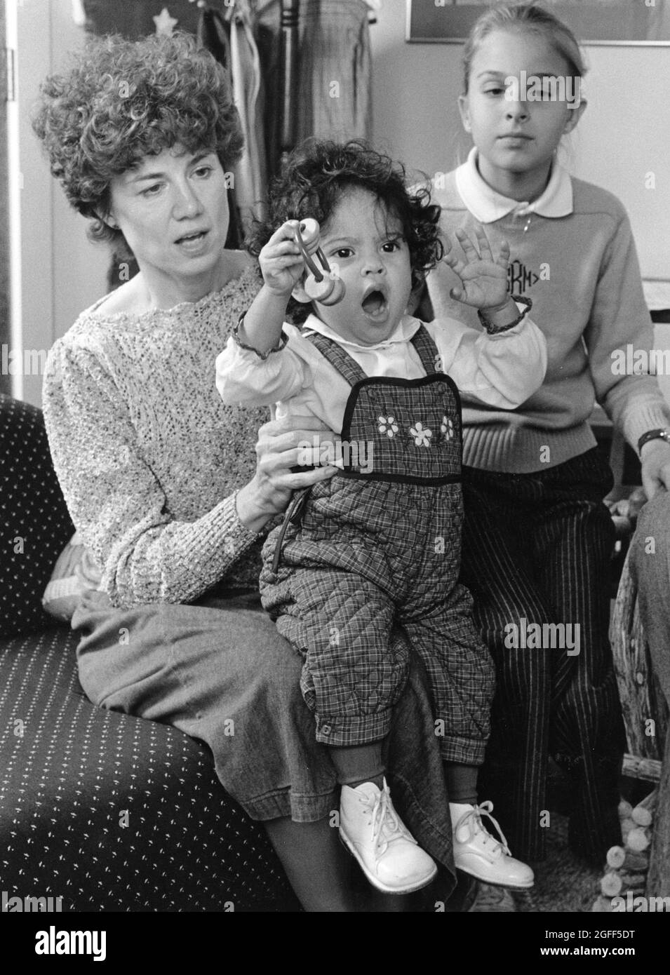 Austin Texas USA, um 1988: Frau hält ihr adoptiertes honduranisches Kind auf dem Schoß, während ihr natürliches Kind aufschaut. ©Bob Daemmrich Stockfoto