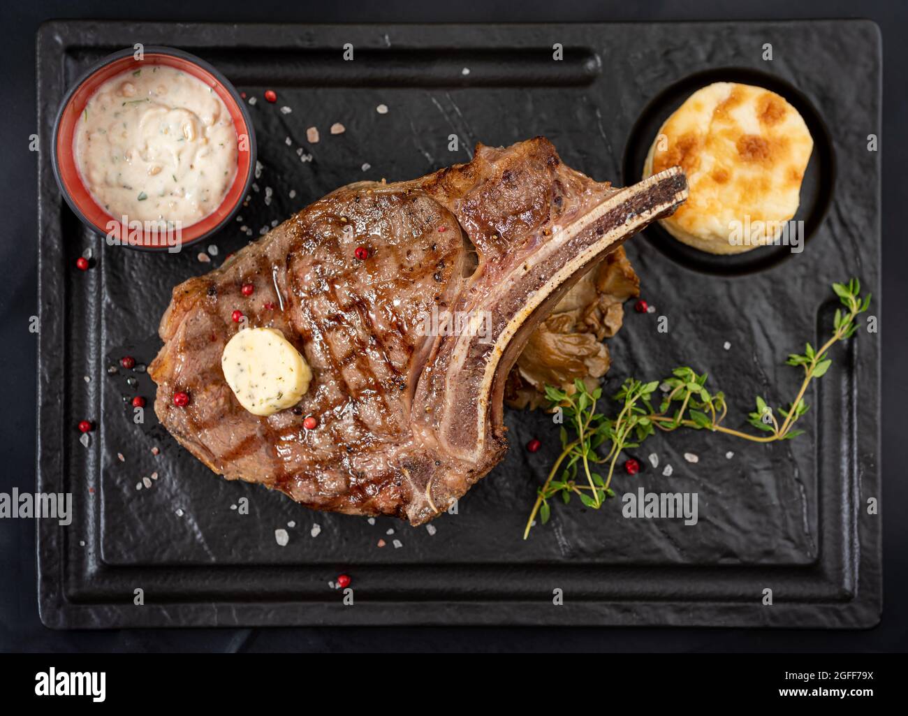 Gegrilltes Kalbsschnitzel auf schwarzem Steinteller mit Sauce und Garnitur. Stockfoto