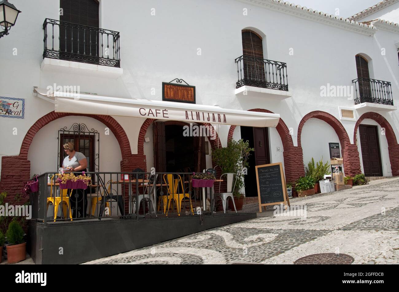 Blick auf die Straße mit Café, Frigiliana, Provinz Malaga, Andalusien, Spanien. Frigiliana ist eine kleine Stadt in der Nähe von Nerja, aber in den Bergen und bekannt als eins Stockfoto