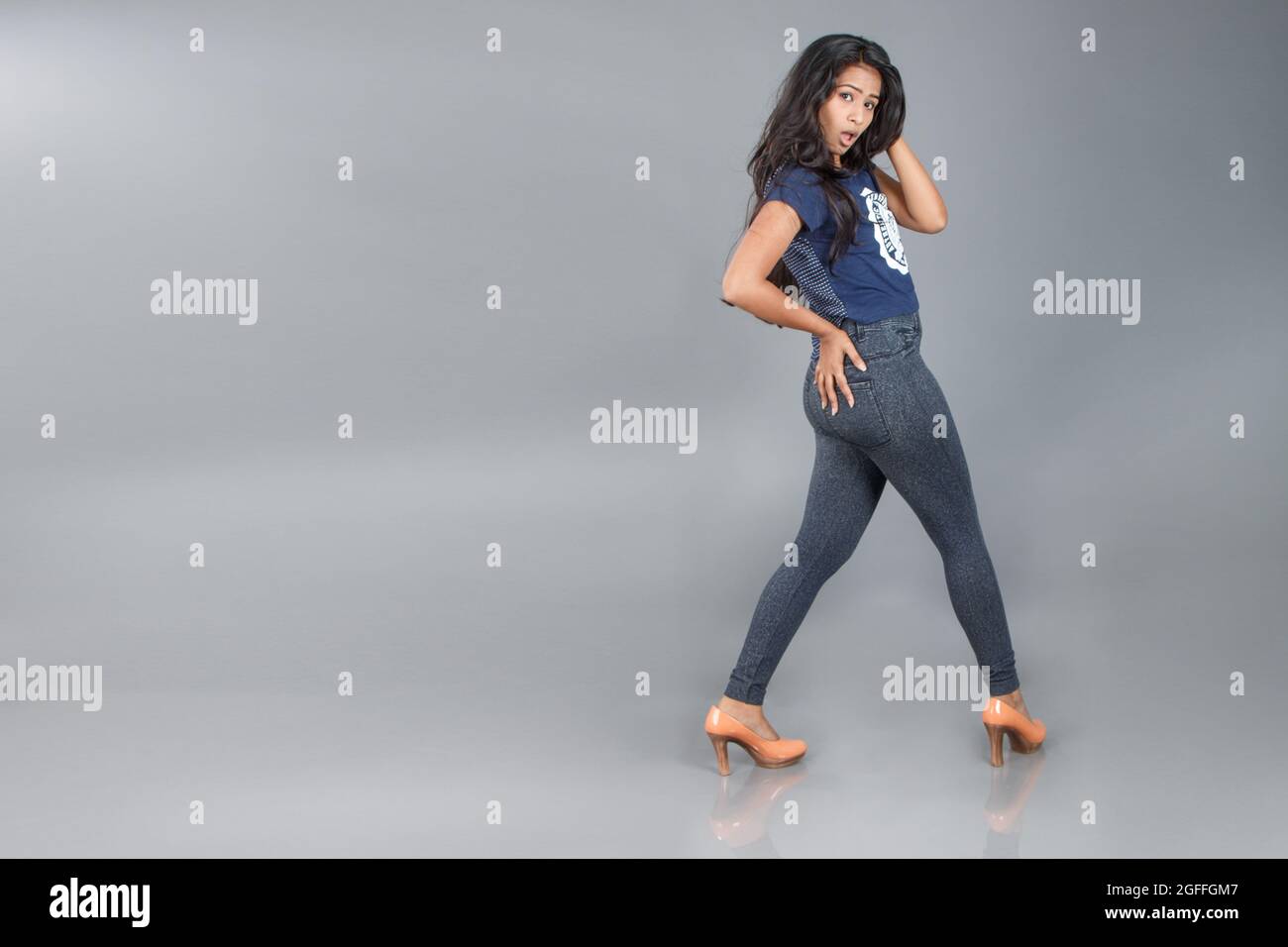 Ein schönes junges Mädchen, das vor grauem Hintergrund tanzt und mit ihren Schuhen als Modelin spielt Stockfoto