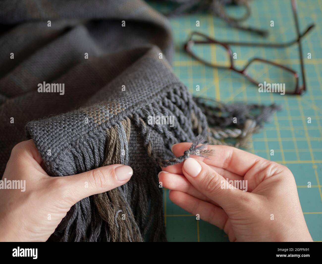 Handwerker ist in Aktion. Die Frau kreiert einen Fransen auf einem Wollschal oder Schalldämpfer. Hände von Handwerkern mit gewebtem Produkt Stockfoto