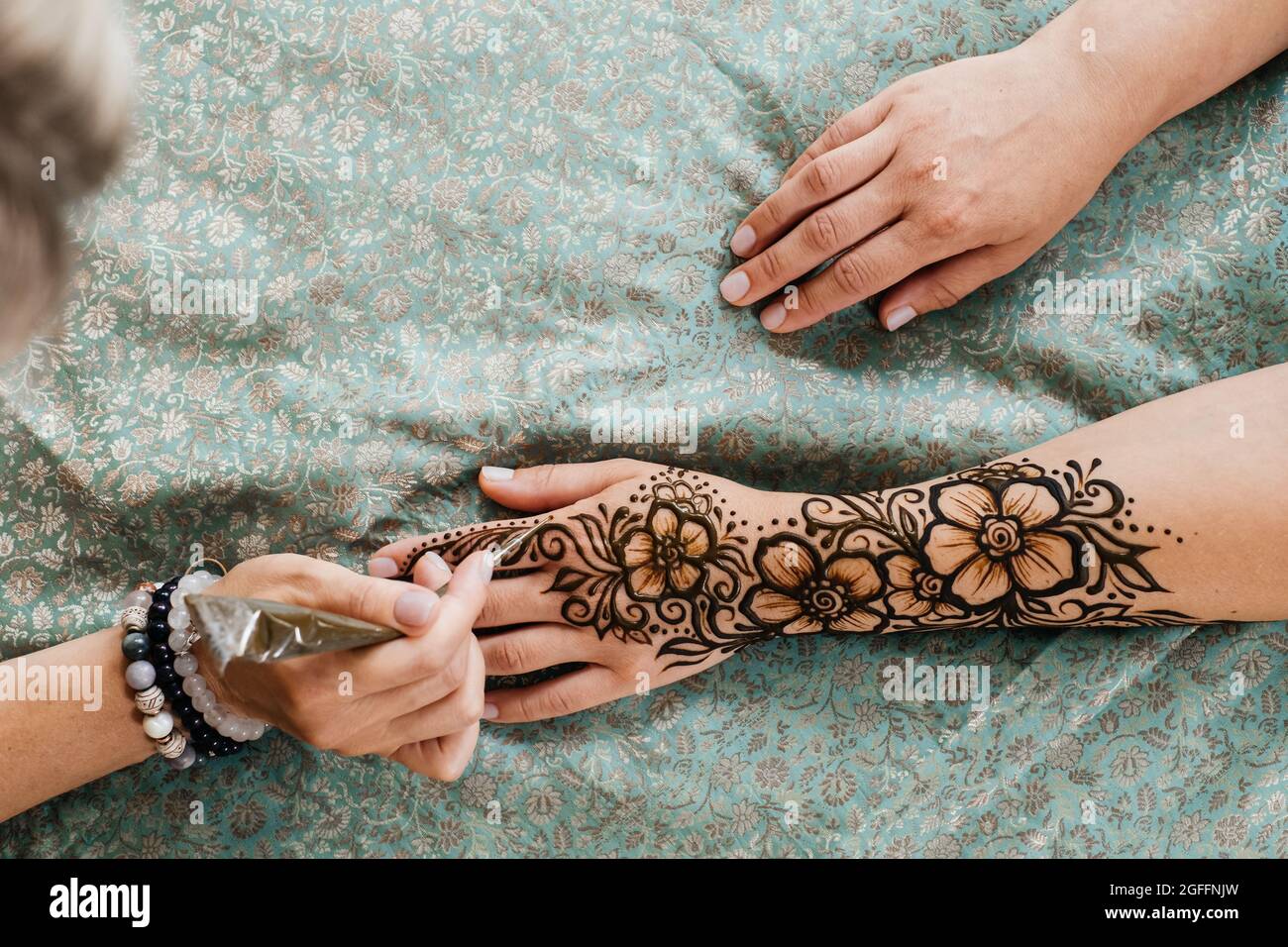 Künstlerin, die Henna-Tätowierung auf Frauenhänden anwendet. Mehndi ist traditionelle indische dekorative Kunst, Hand mit floralen Mehendi. Beauty-Zeichnung für Hochzeiten und Stockfoto