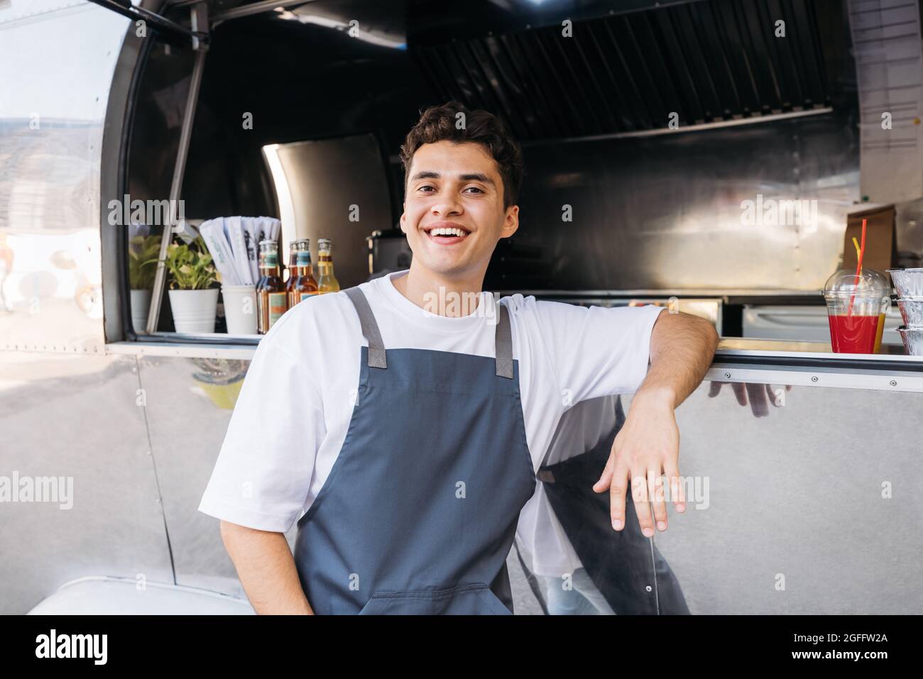 Porträt eines glücklichen Besitzers eines Food-Trucks. Typ aus dem Nahen Osten im Vorfeld, der sich auf einen Food Truck lehnte und die Kamera ansah. Stockfoto
