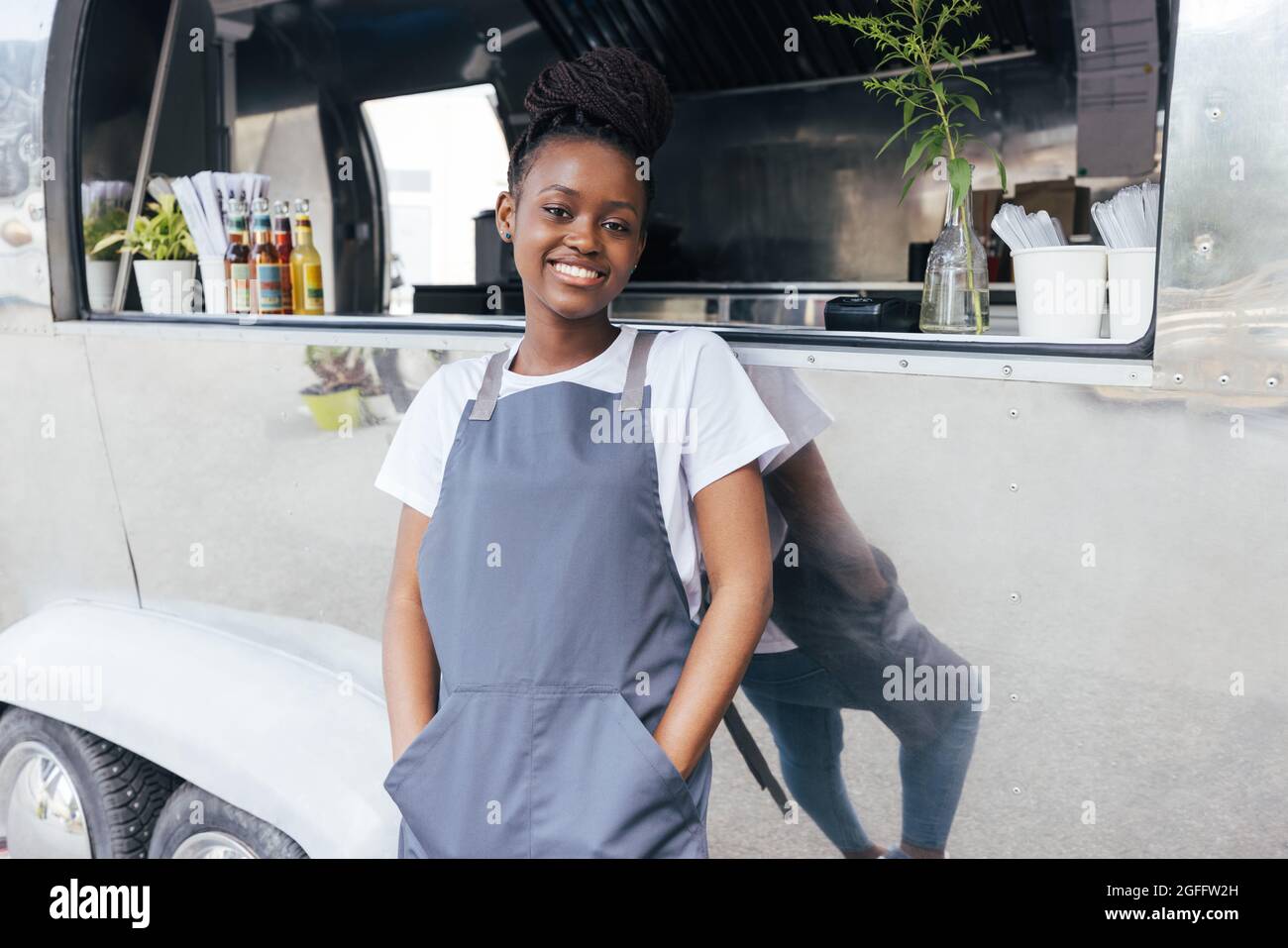 Porträt einer lächelnden Besitzerin auf der Schürze, die sich auf einen Food Truck stützt und die Kamera anschaut Stockfoto