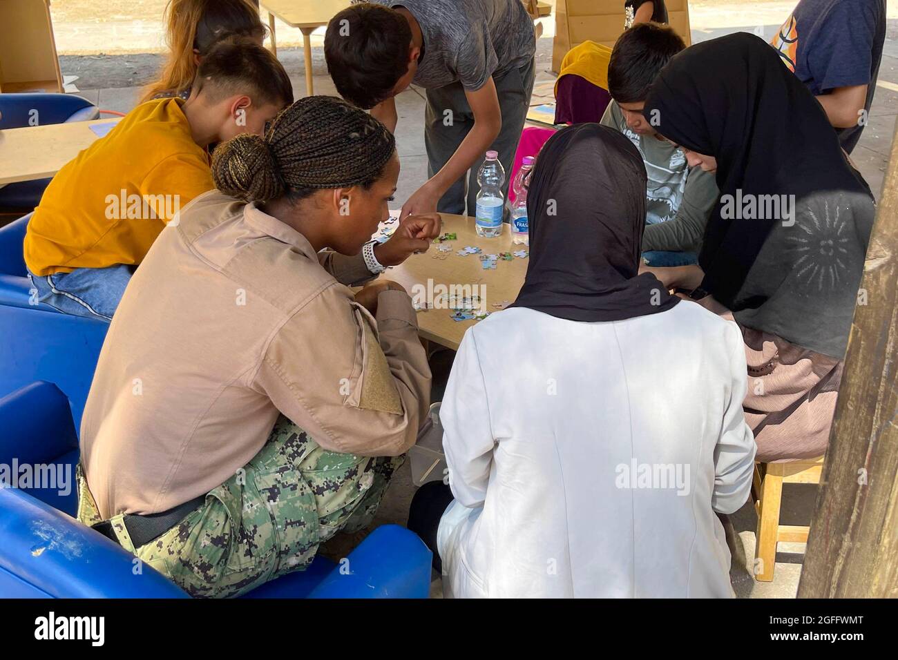 Ein Seemann der United States Navy und afghanische Kinder, die evakuiert wurden, stellten Puzzles auf der Naval Air Station Sigonella zusammen, 24. August 2021. NAS Sigonella unterstützt die Mission “Operation Allies Refuge des Verteidigungsministeriums, um die sichere Ausreise und Umsiedlung von US-Bürgern, Empfängern von Sondervisa für Immigration und gefährdeten afghanischen Bevölkerungen aus Afghanistan zu erleichtern. Obligatorische Gutschrift: Kevin Pickard, Jr./US Navy über CNP Stockfoto