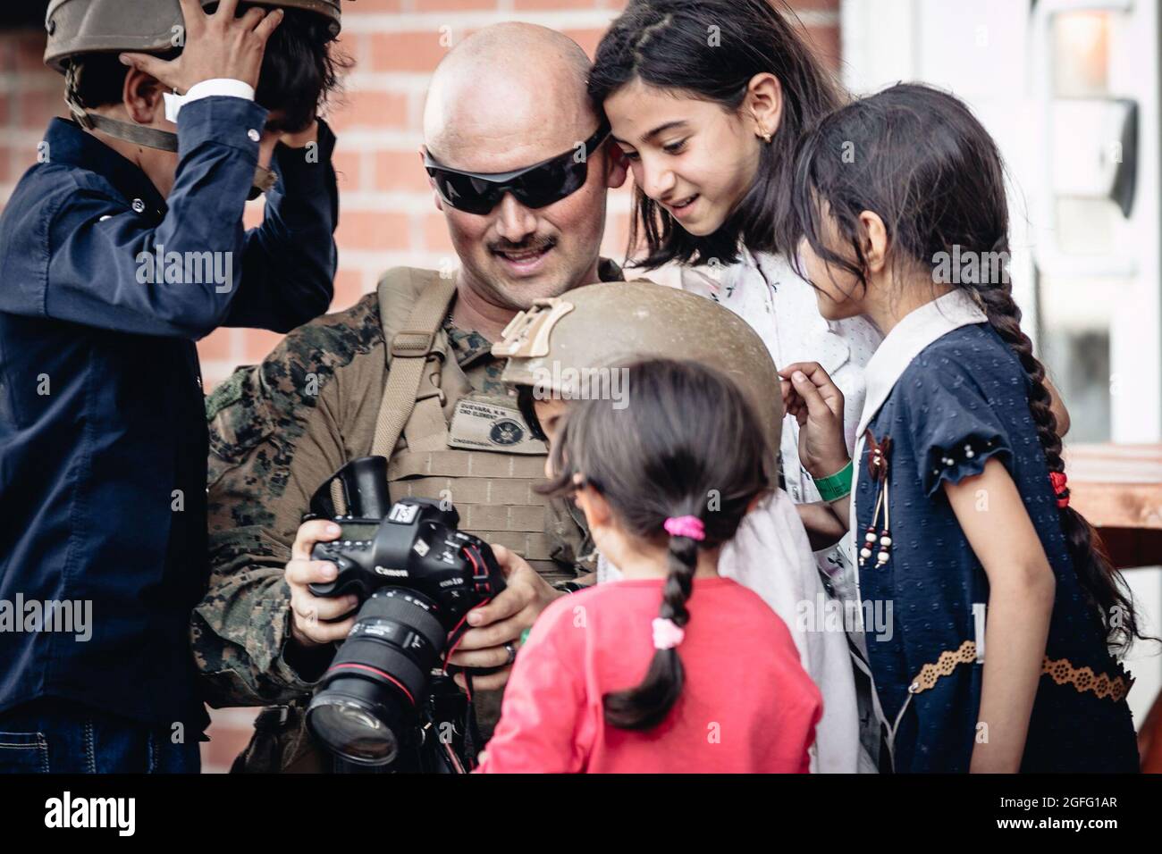 Eine US-Marine, die der 24. Marine Expeditionary Unit zugeordnet ist, zeigt ihre Kamera Kindern, die auf die Evakuierung warten, am Hamid Karzai International Airport, Afghanistan, 24. August 2021. Die USA unterstützen das Außenministerium bei einer nicht-kombatanten Evakuierungsoperation (NEO) in Afghanistan. Quelle: Melissa Marnell/US Marine Corps via CNP /MediaPunch Stockfoto