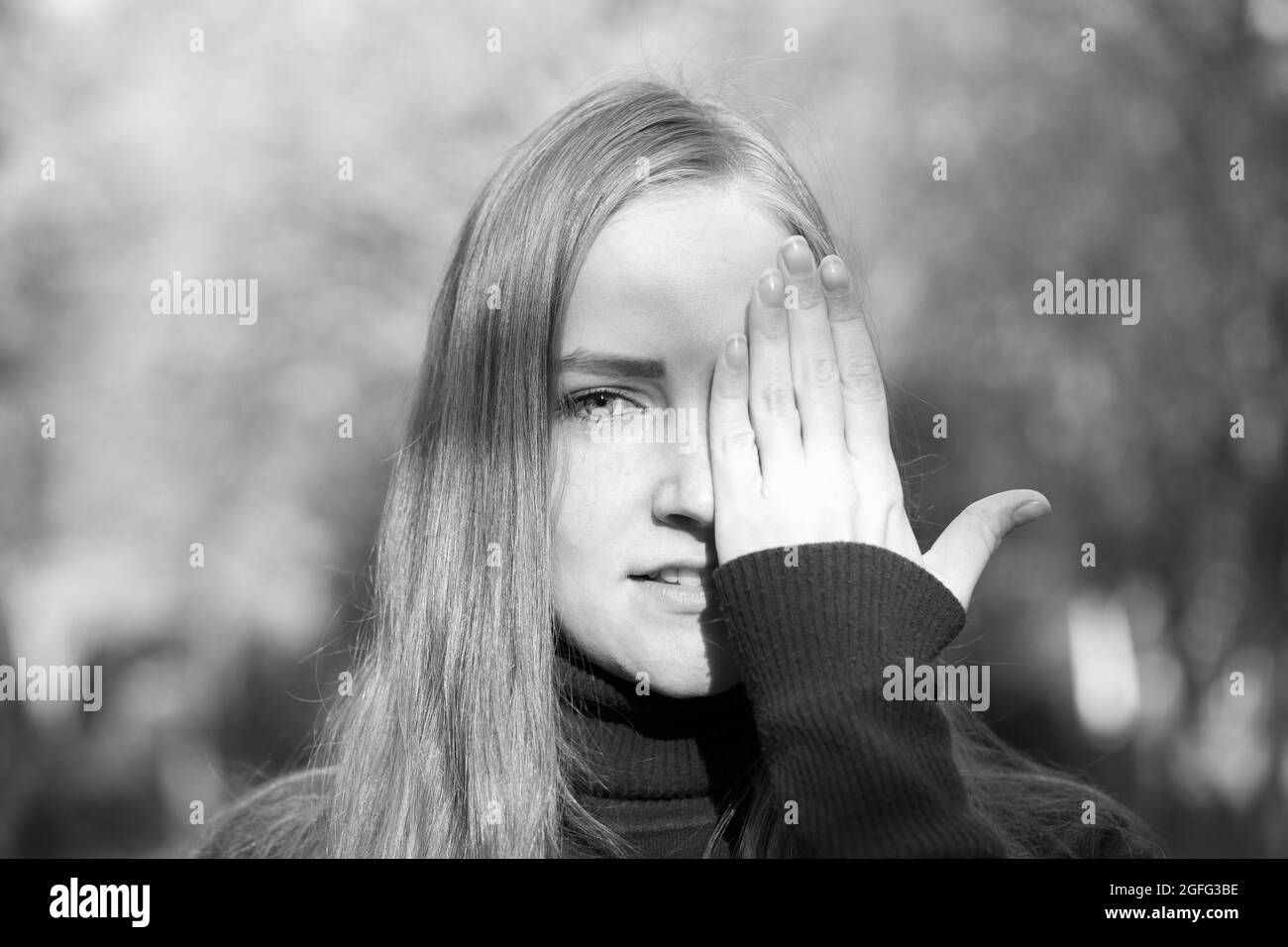 Schöne junge Frau auf einem Hintergrund von Herbstbäumen. Emotionskonzept. Das Mädchen bedeckt ihr Gesicht mit der Hand. Stockfoto