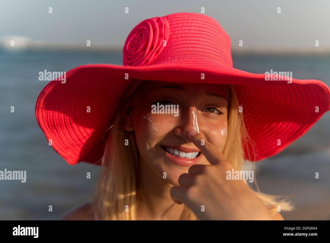 Teenager Mädchen in rosa Hut verbreiten Sonnencreme und lachen. Stockfoto