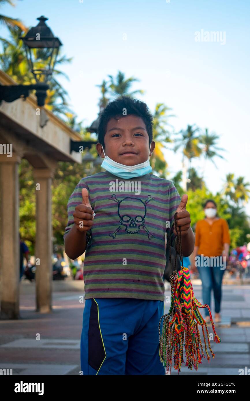 Ryohacha, La Guajira, Kolumbien - Mai 26 2021: Porträt eines Wayuu-Jungen in einem gestreifte T-Shirt, trägt eine Maske unter seinem Mund und schaut auf das C Stockfoto