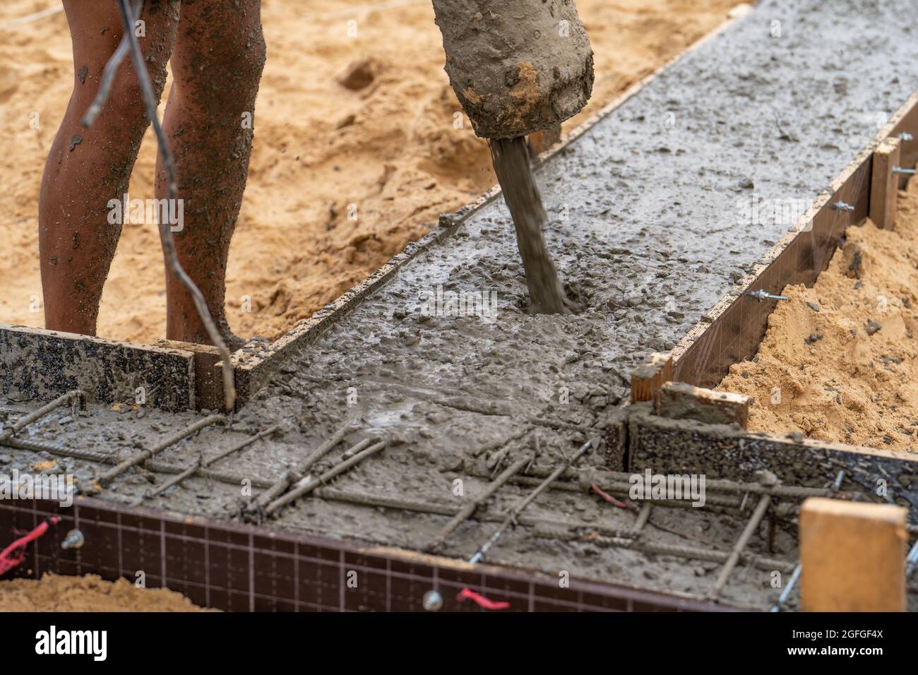 Ausgießen von Fertigbeton in Schalung mit Bewehrung. Nasser Zement fließt in das Fundament des zivilen Gebäudes, aus nächster Nähe. Stockfoto