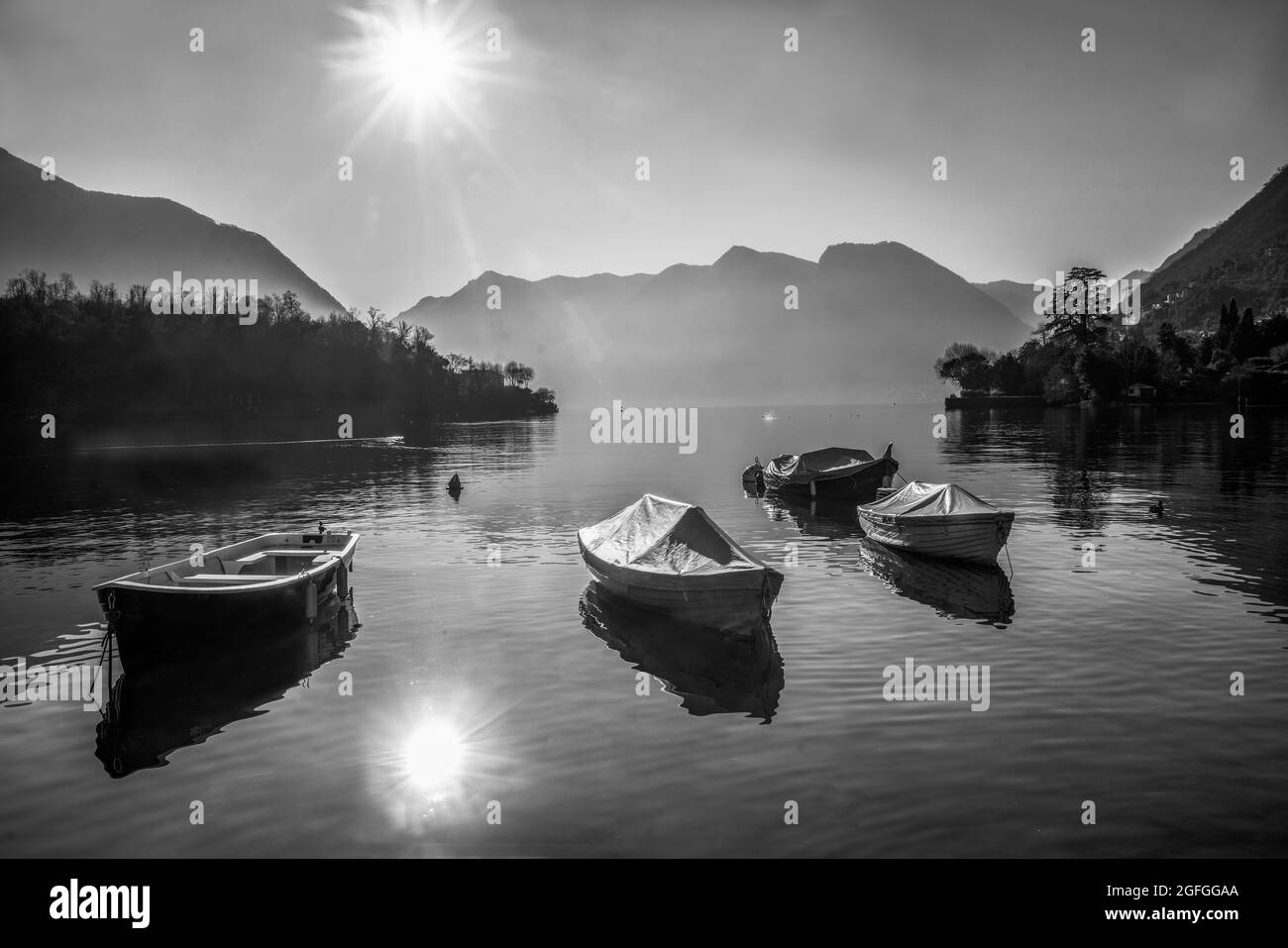 Erstaunliches Comer See-Panorama: Sonniger Tag im Winter. Ummantelte Boote im Wasser in der Nähe der Küste, Ducka Schwimmen. Berge und Häuser von italienischen Dörfern a Stockfoto