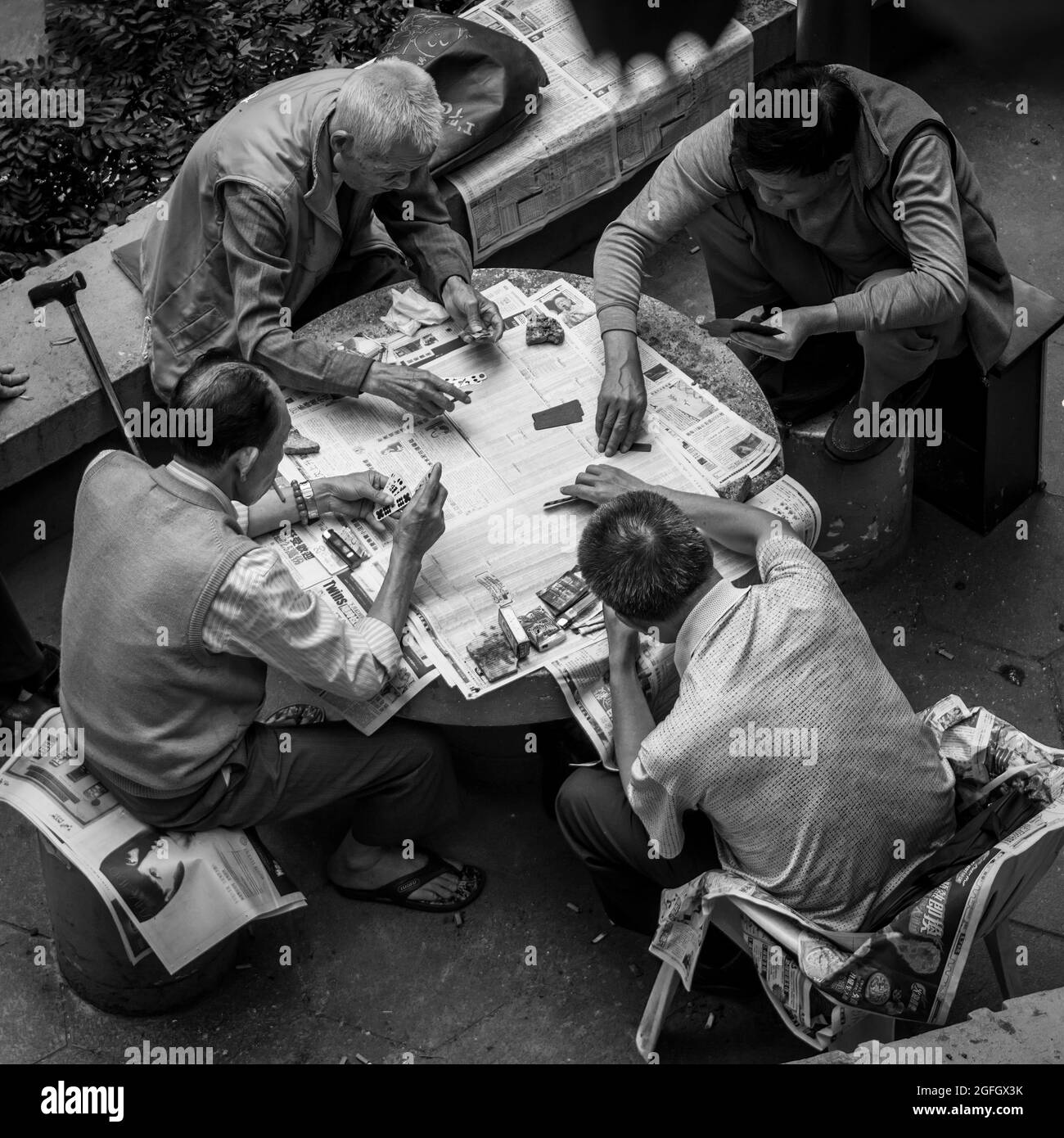 Vier chinesische Männer spielen in einem öffentlichen „Ausgehen“-Bereich in Wan Chai, Hong Kong Island, mit Spielkarten (monochrom) Stockfoto