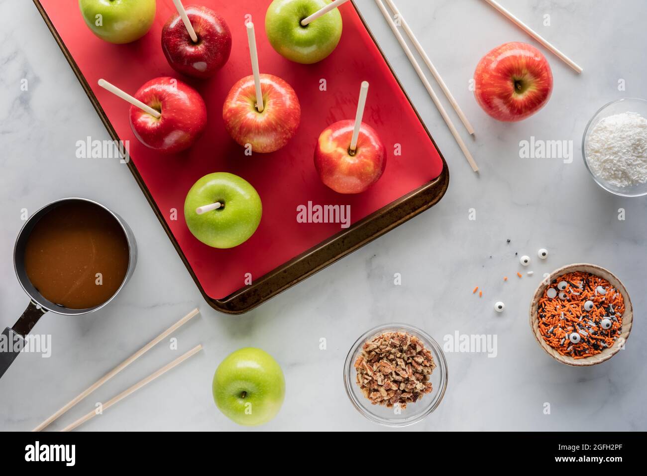 Draufsicht auf Äpfel in einer Pfanne, die von Zutaten umgeben ist, um Karamelläpfel für Halloween zu machen. Stockfoto