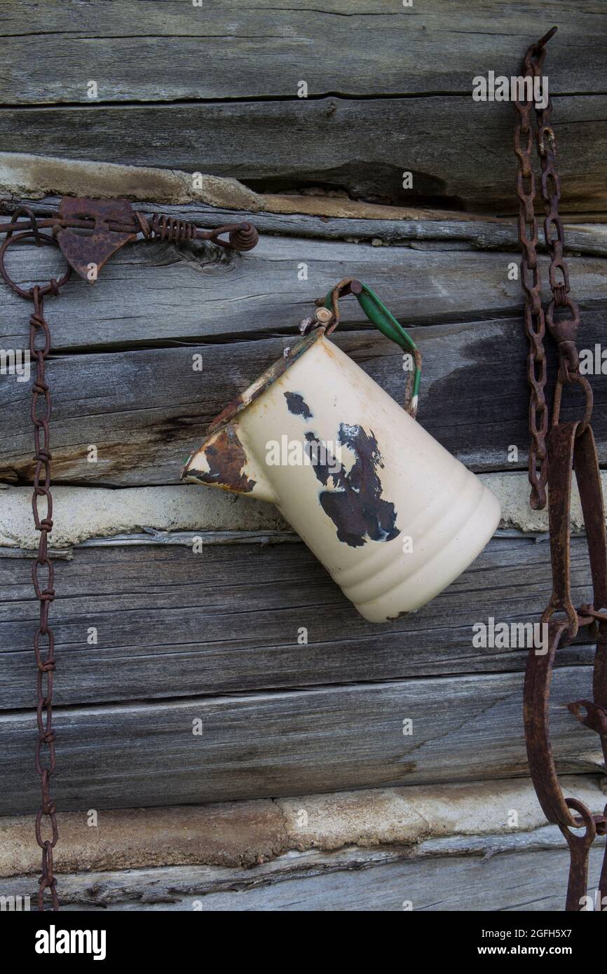 Eine alte, verrostete Porzellankaffeepfanne zeigt die Abnutzung des harten Gebrauchs. An der Wand einer Blockhütte. Stockfoto