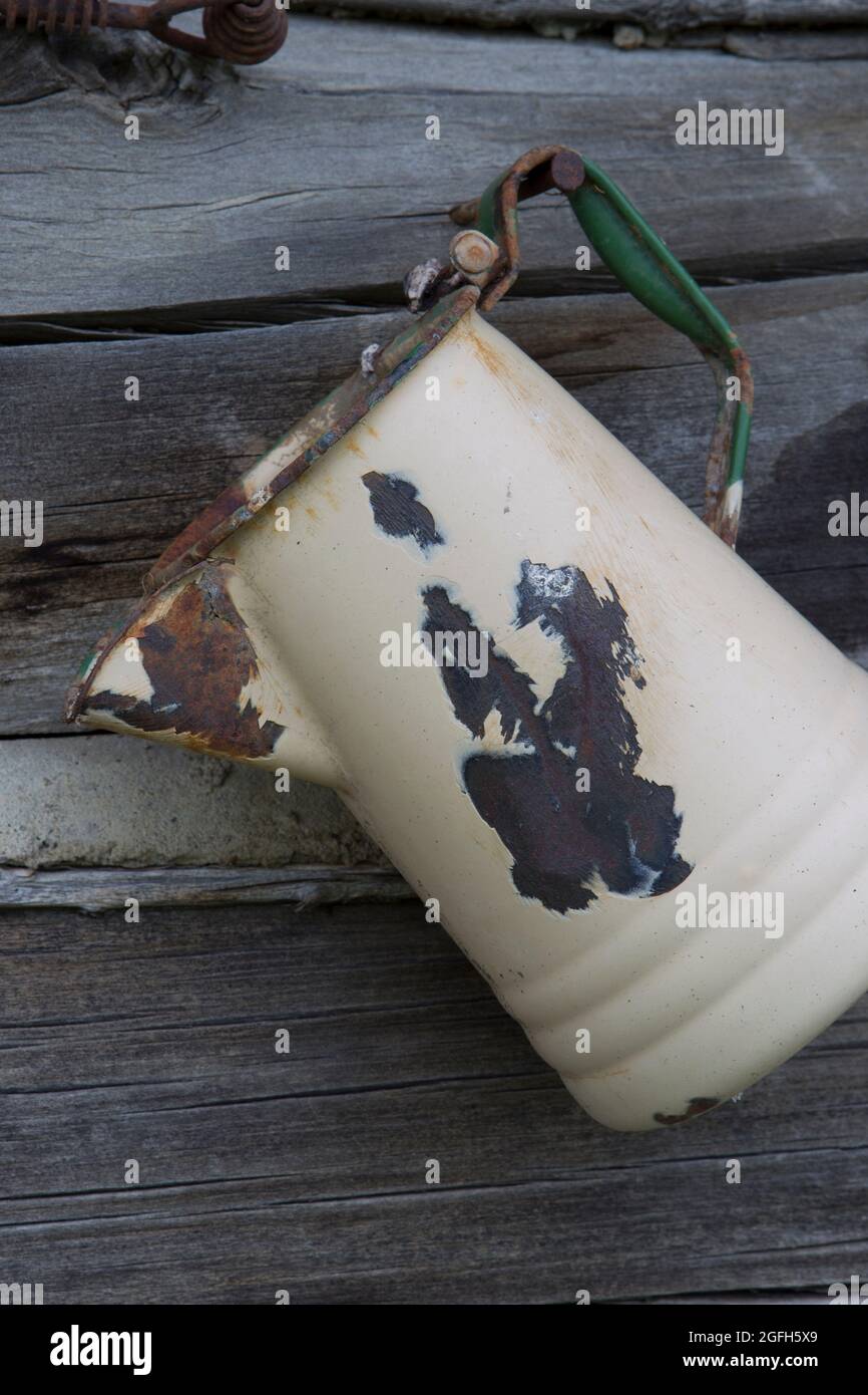 Eine alte, verrostete Porzellankaffeepfanne zeigt die Abnutzung des harten Gebrauchs. An der Wand einer Blockhütte. Stockfoto