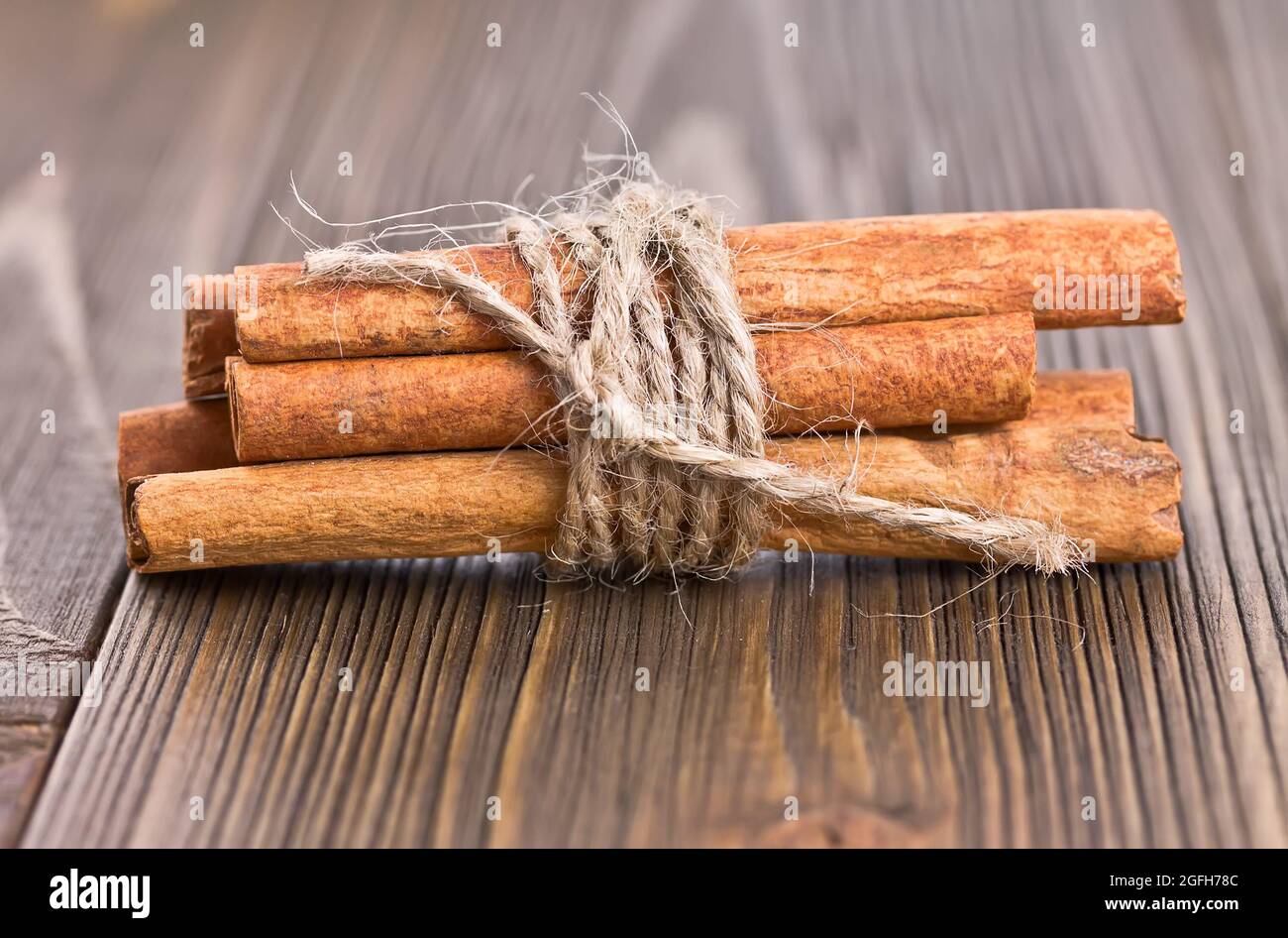 Einige Zimtstangen, die mit Garn auf einem alten Holzbrett gebunden sind Stockfoto