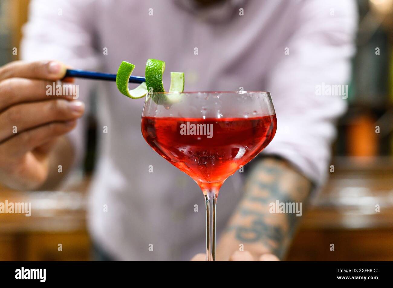 Nahaufnahme eines Glases mit rotem Getränk, das der Barkeeper mit Orangenschale akkurat dekorieren kann Stockfoto