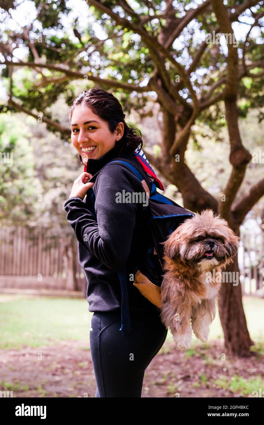 Eine charmante junge Frau geht in der Natur, mit einem Rucksack auf der Schulter, aus dem ihr Hund herausschaut. Konzept Beziehung und Liebe zu Tieren Stockfoto