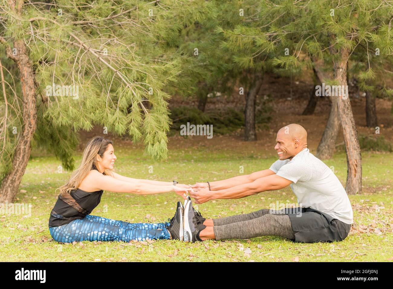 Sportliches Paar macht zusammen Übungen, während es sitzt und die Hände hält Stockfoto