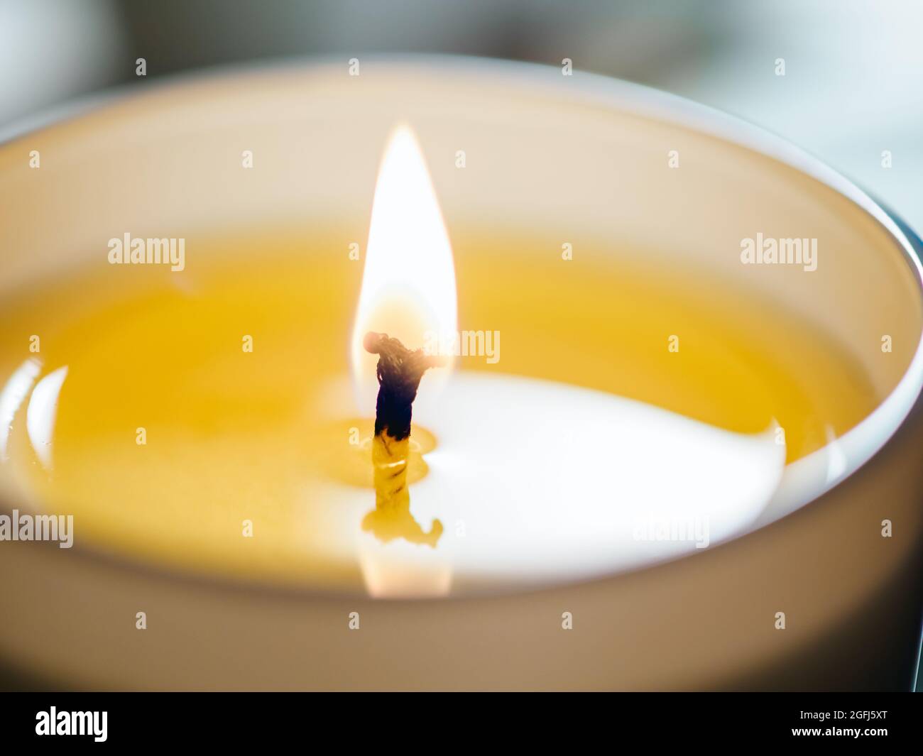 Brennender Kerzendocht mit beigefarbenem Wachs-Nahaufnahme auf hellem Hintergrund. Candle Wick Flame, extrem nahes Foto mit Kopierbereich Stockfoto