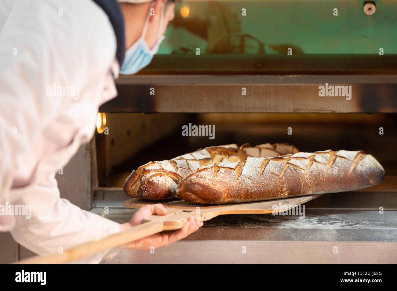 Super U Supermarkt : jemand, der Brot Baker nimmt Bauernbrot aus dem Ofen Stockfoto