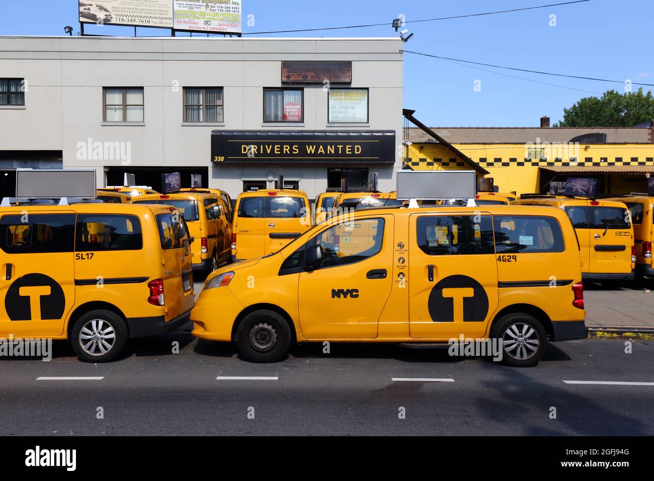 NYC Taxi Taxis parken in einer Taxigarage am McGuinness Blvd in Greenpoint, Brooklyn, mit einem Schild mit der Aufschrift „Fahrer gesucht“ im Hintergrund. 31. Juli 2021. Stockfoto