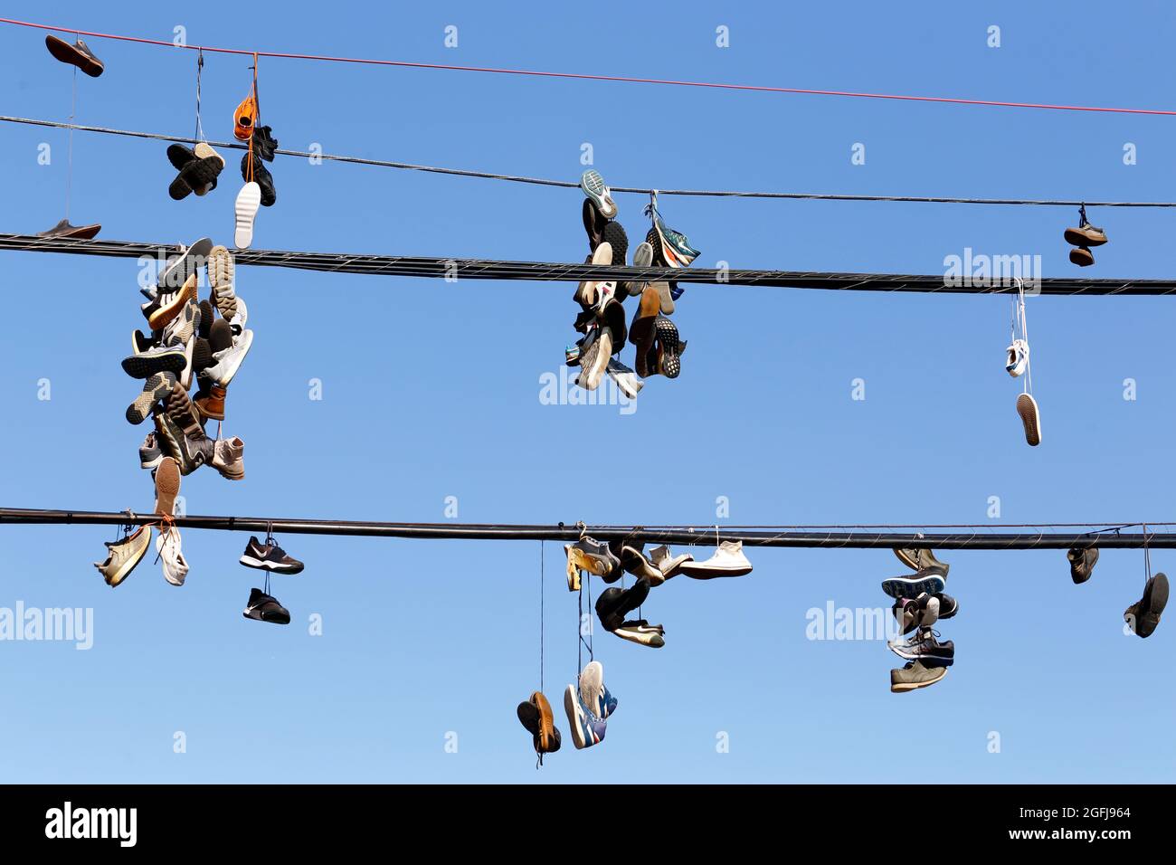 Shoeffiti, Sneakers, die am Telefonkabel an einem sonnigen blauen Himmel hängen; Sneakers, die zusammengebunden sind und über eine Stromleitung geschleudert werden. Stockfoto