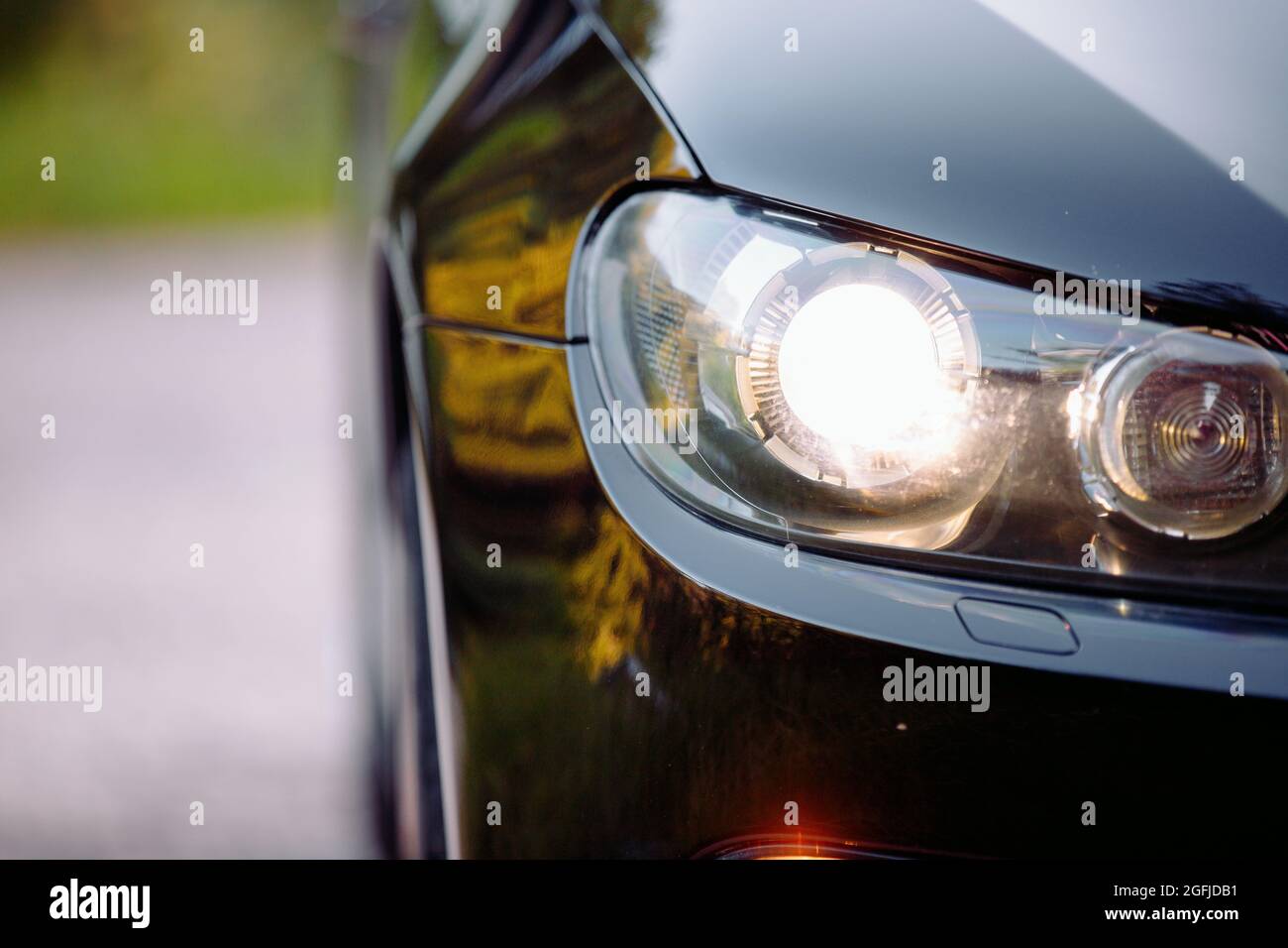 Zugeschnittenes Foto eines schönen, glänzenden schwarzen Automobils auf der Straße mit eingeschalteten Scheinwerfern, Nebelscheinwerfern und einem Teil eines Rades. Stockfoto