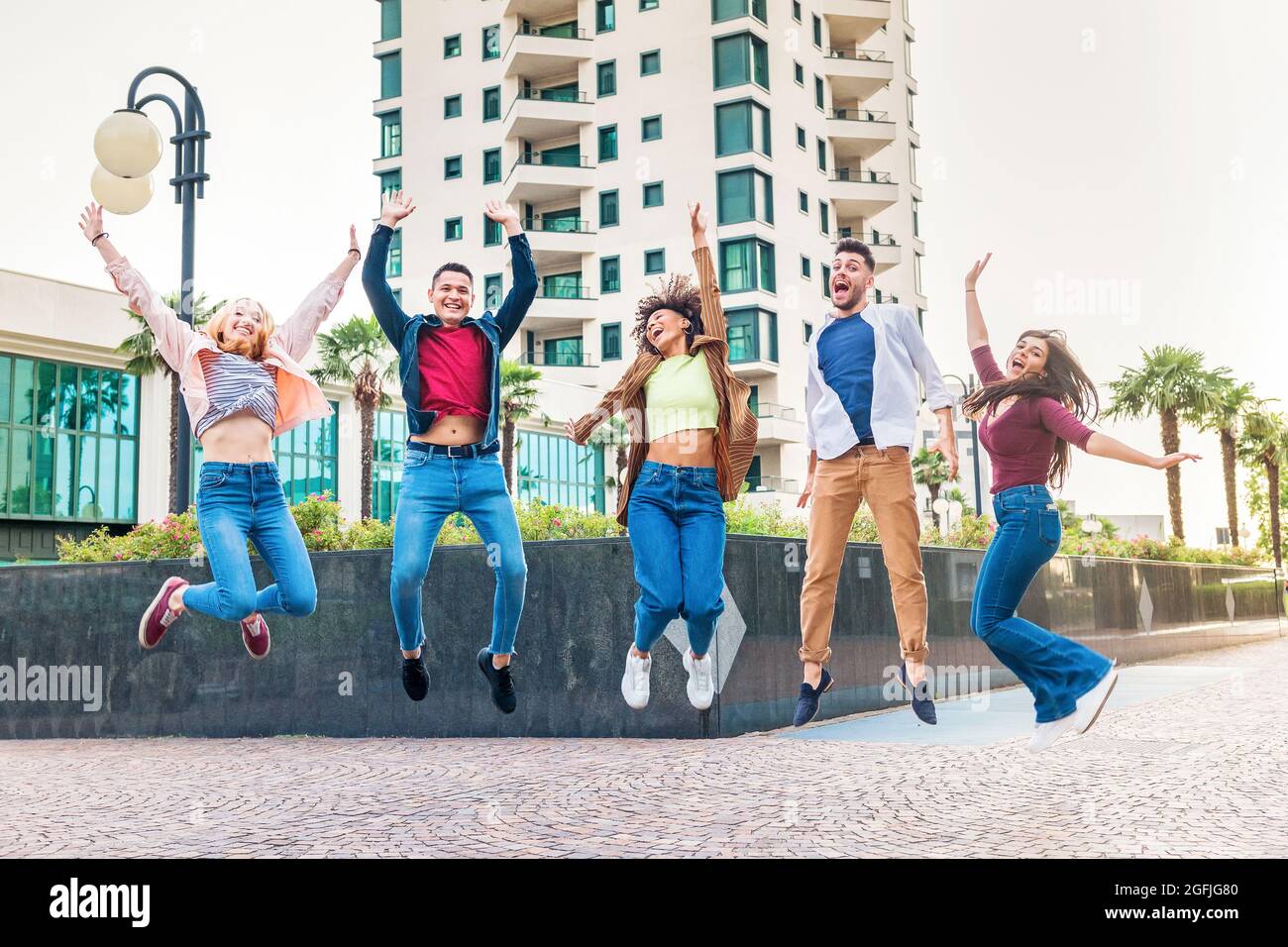 Eine Gruppe ausgelassener, vielfältiger junger Freunde, die in der Luft in einer Stadtstraße springen und vor Freude jubeln und lachen, während sie gemeinsam feiern Stockfoto