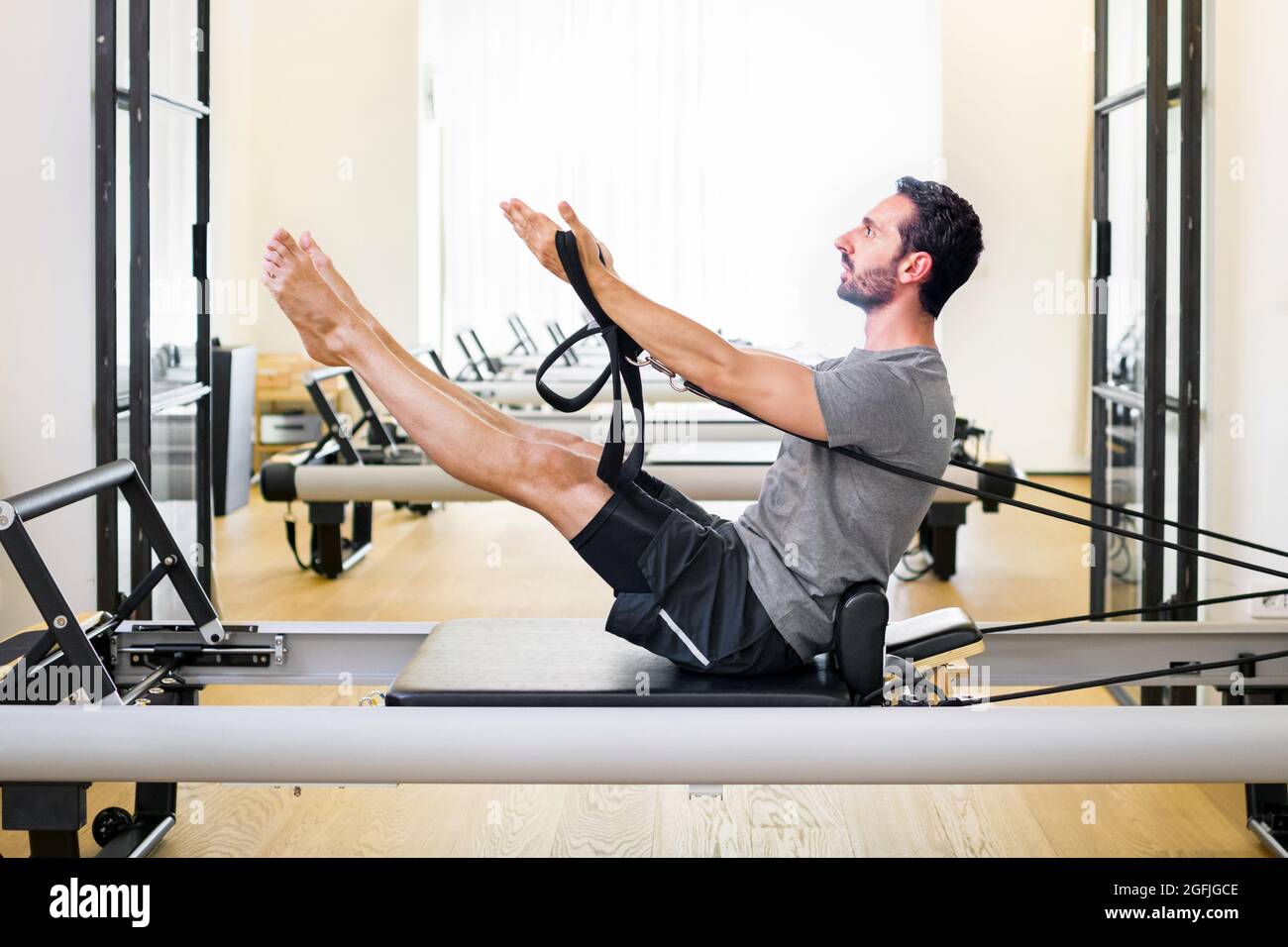 Fit muskulösen Mann tun einen Teaser pilates Übung auf einem Reformer in einer Turnhalle, um seine Kern-und Bauchmuskeln in einer Seitenansicht mit Copyspace zu stärken Stockfoto