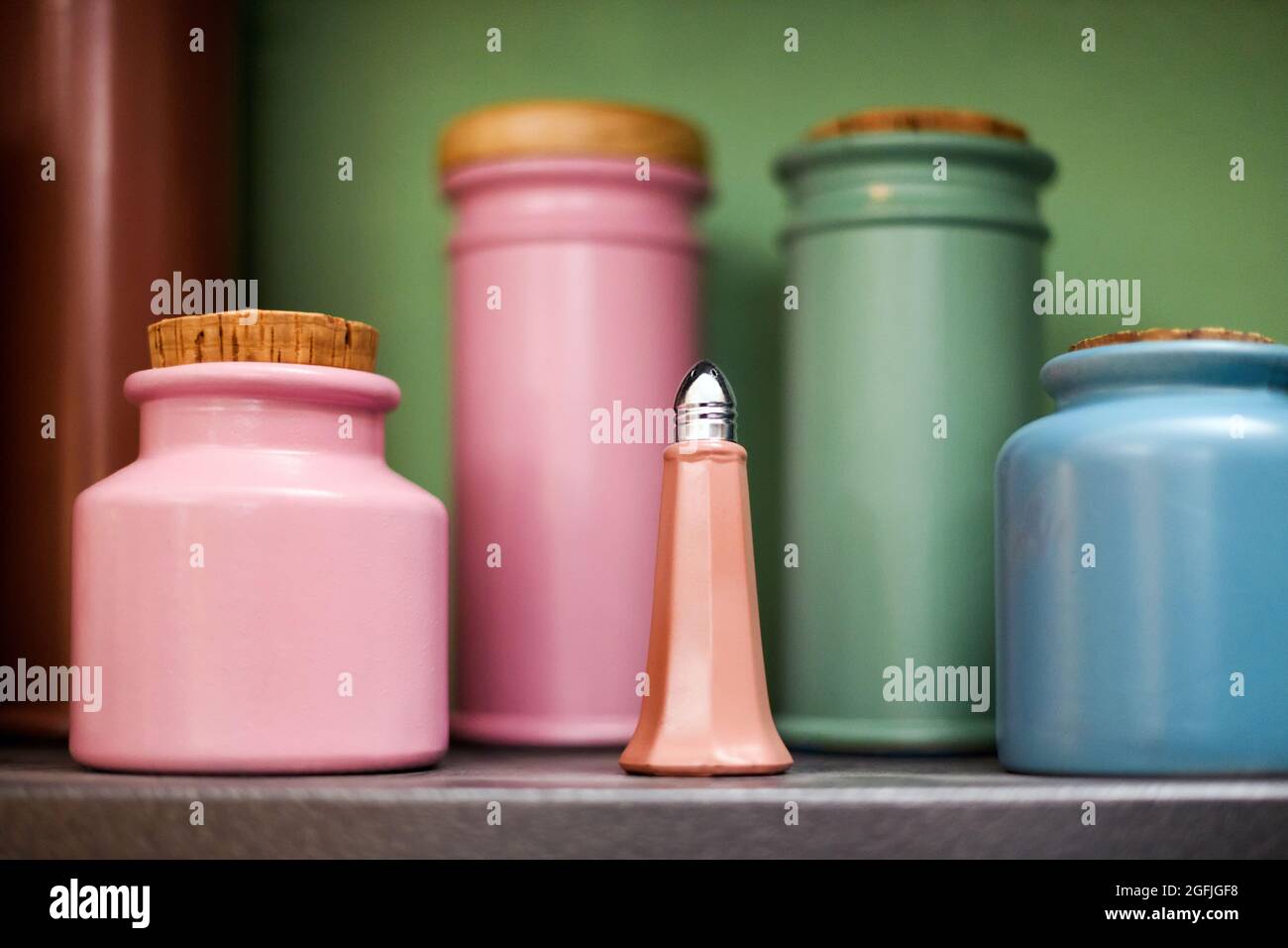 Auswahl an bunten handgefertigten Keramik- oder Töpferkitchenbehältern auf einem Regal mit selektivem Fokus auf einen rosa Salzstreuer im Vordergrund in der Nähe Stockfoto