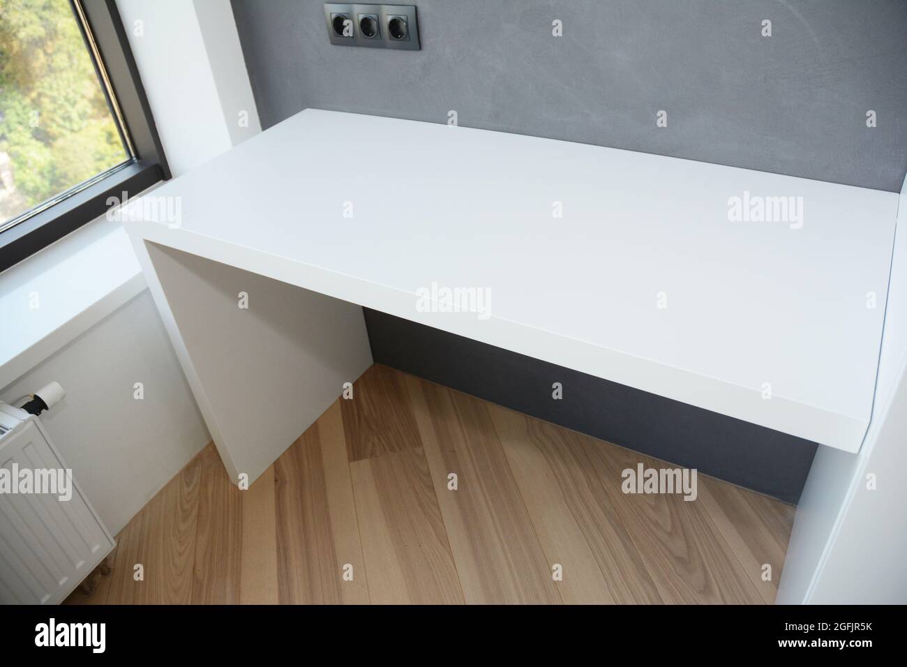 Ein Computertisch mit weißem Glanz auf dem Holzlaminatboden in der Nähe des  Fensters mit Heizkörper und lackierter grauer Wand mit schwarzen  europäischen Wandmontierern Stockfotografie - Alamy
