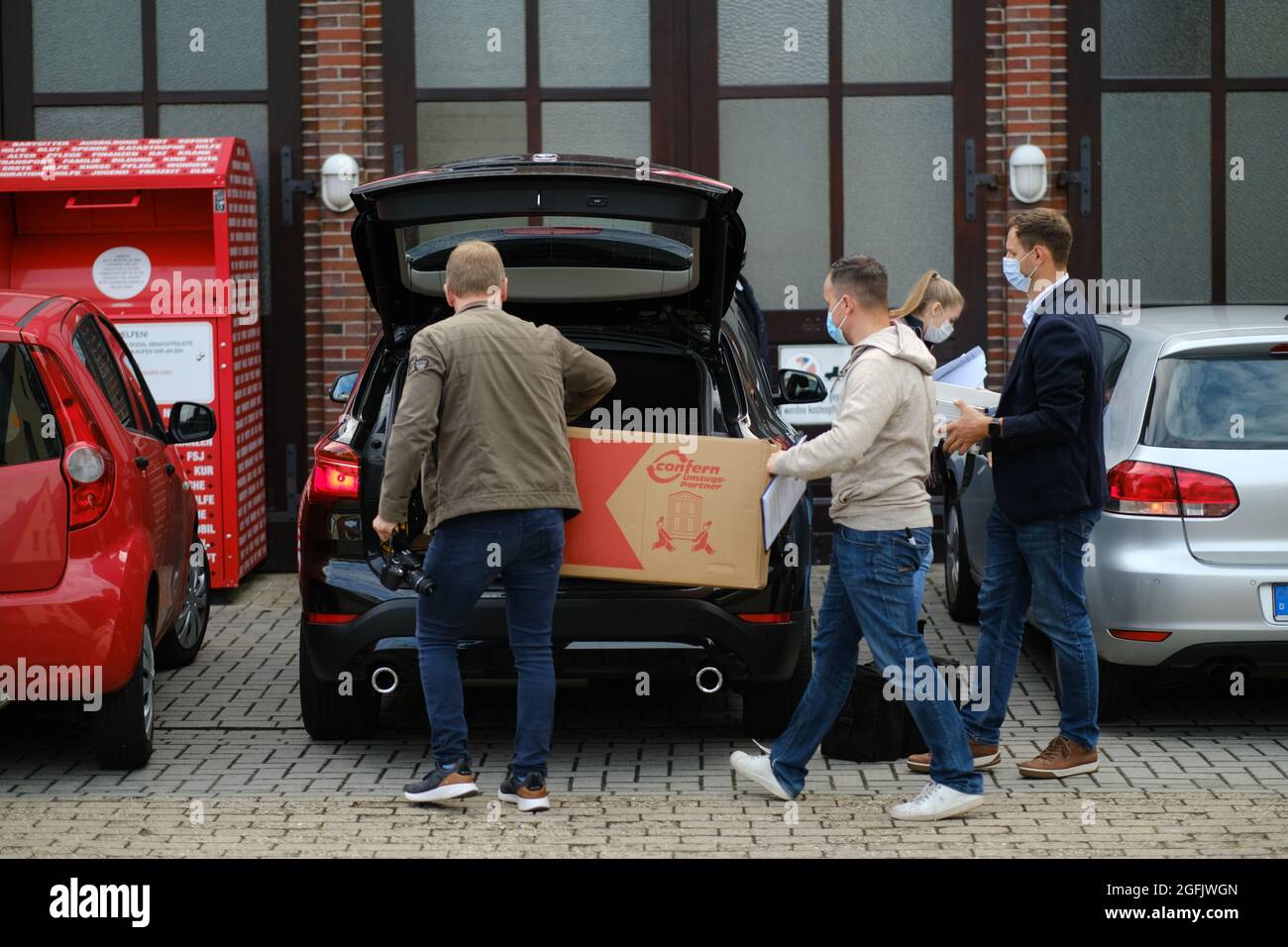 Varel, Deutschland. August 2021. Zivile Polizisten tragen Kisten in ein ziviles Polizeifahrzeug vor dem DRK-Gebäude. In den Morgenstunden durchsuchten Beamte mehrere Gebäude des Deutschen Roten Kreuzes (DRK) in Friesland. Der Soko 'Vakzin' fand während seiner Ermittlungen weitere Unregelmäßigkeiten. (To dpa 'Suchvorgänge während der Untersuchung von Kochsalzeinspritzungen') Quelle: Markus Hibbeler/dpa/Alamy Live News Stockfoto