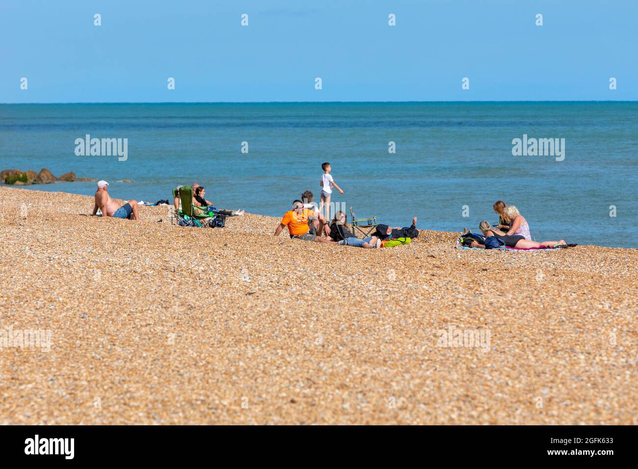 Familiengruppen entspannen sich an einem Kiesstrand am Meer in der Abendsonne. Stockfoto