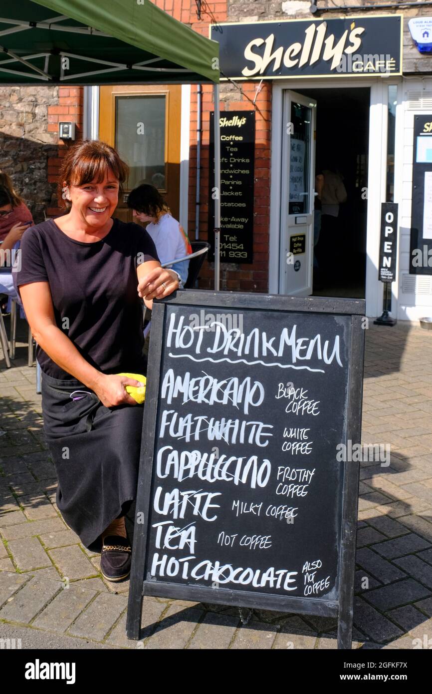 Thornbury, Glos, Großbritannien. August 2021. Café A-Board übersetzt Namen von Modern Coffee in solche, die vor kurzem bekannt gewesen wären. Shelly's ist ein unabhängiges Café, das bei Einheimischen wegen gutem Essen und einem freundlichen Herzlich Willkommen. beliebt ist Abgebildet ist die geschätzte Mitarbeiterin Jane Shepard. Kredit: JMF Nachrichten/Alamy Live Nachrichten Stockfoto