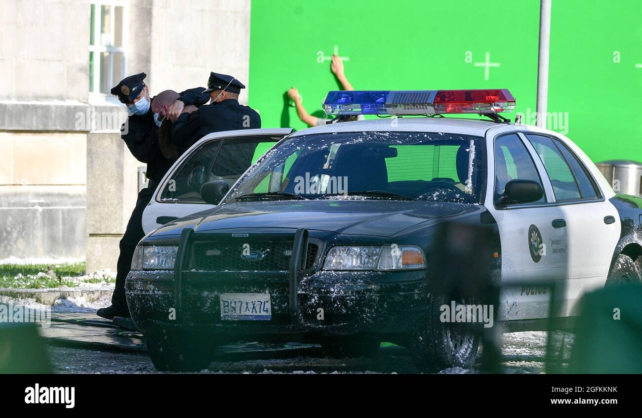 Eine Szene, in der ein Mann aus einem amerikanischen Polizeiauto gezogen wird, wird während der Dreharbeiten zum Netflix-Film Havoc mit Tom Hardy in Swansea eingeprobt. Stockfoto