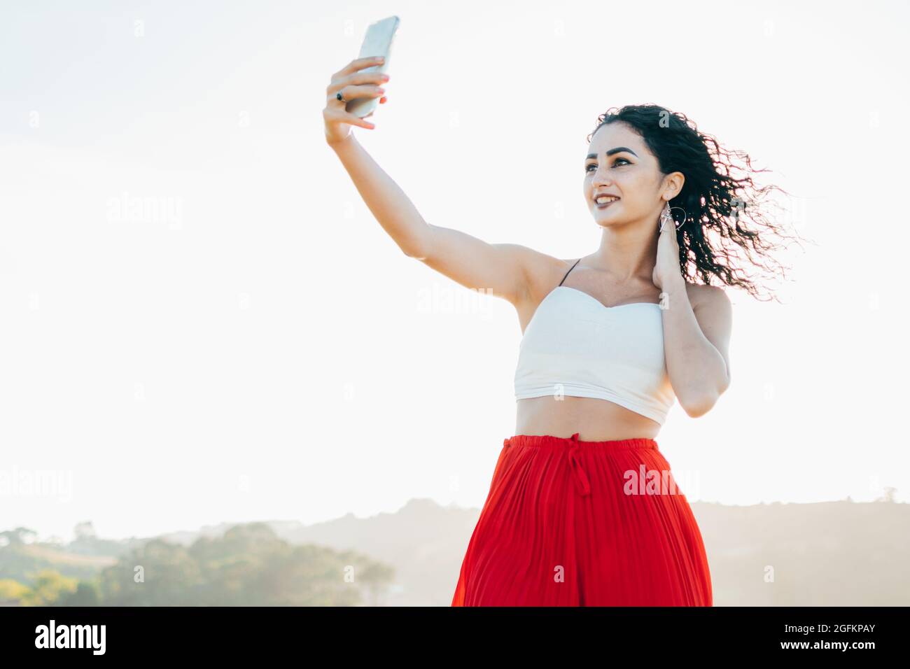 Ein ehrliches Porträt einer stilvollen jungen Frau, die ein Selfie mit dem Mobiltelefon macht und für soziale Medien in einem Park im Freien posiert. Stockfoto
