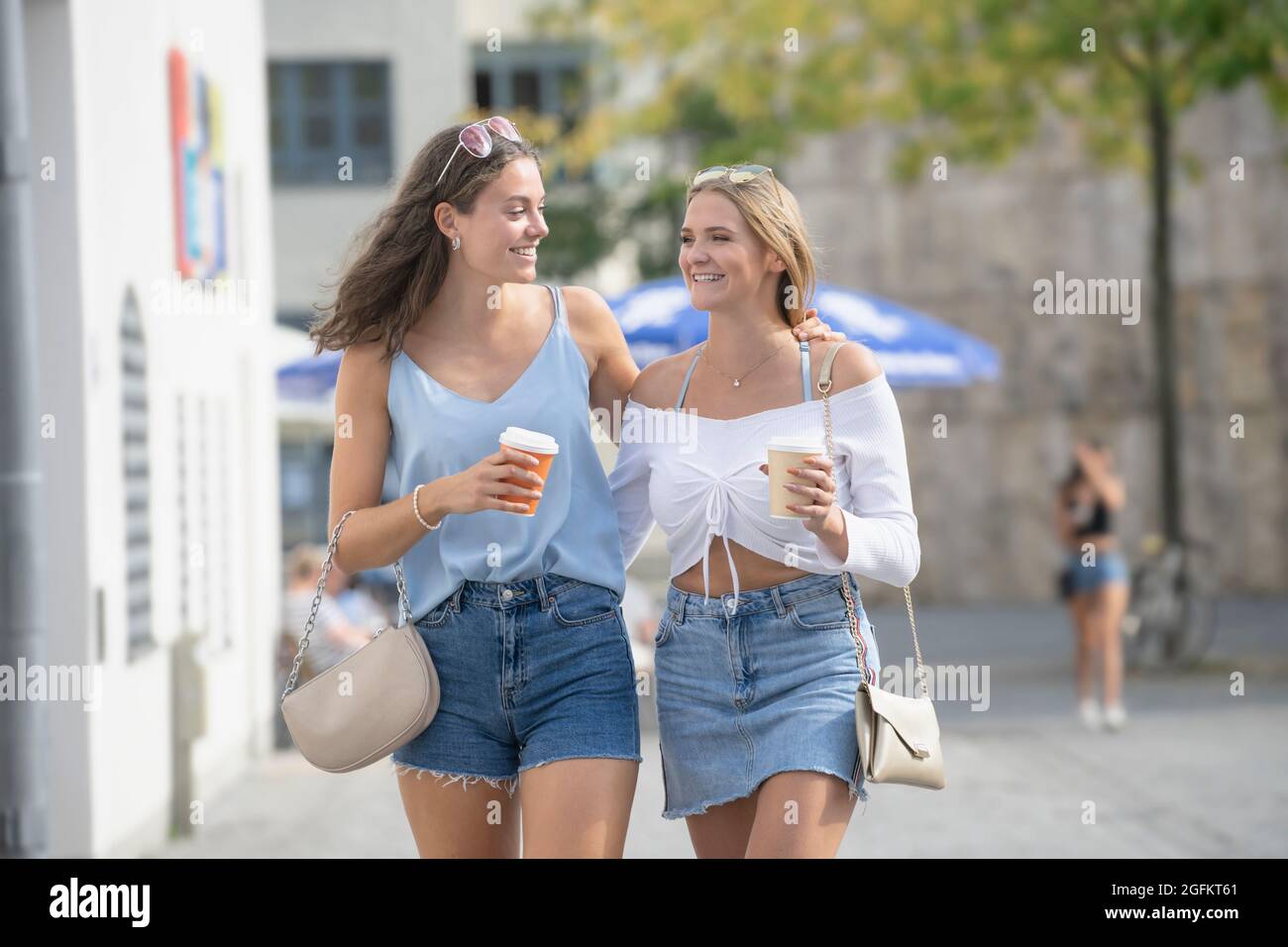 Zwei junge Frauen, die mit Kaffeetassen in der Stadt München spazieren Stockfoto