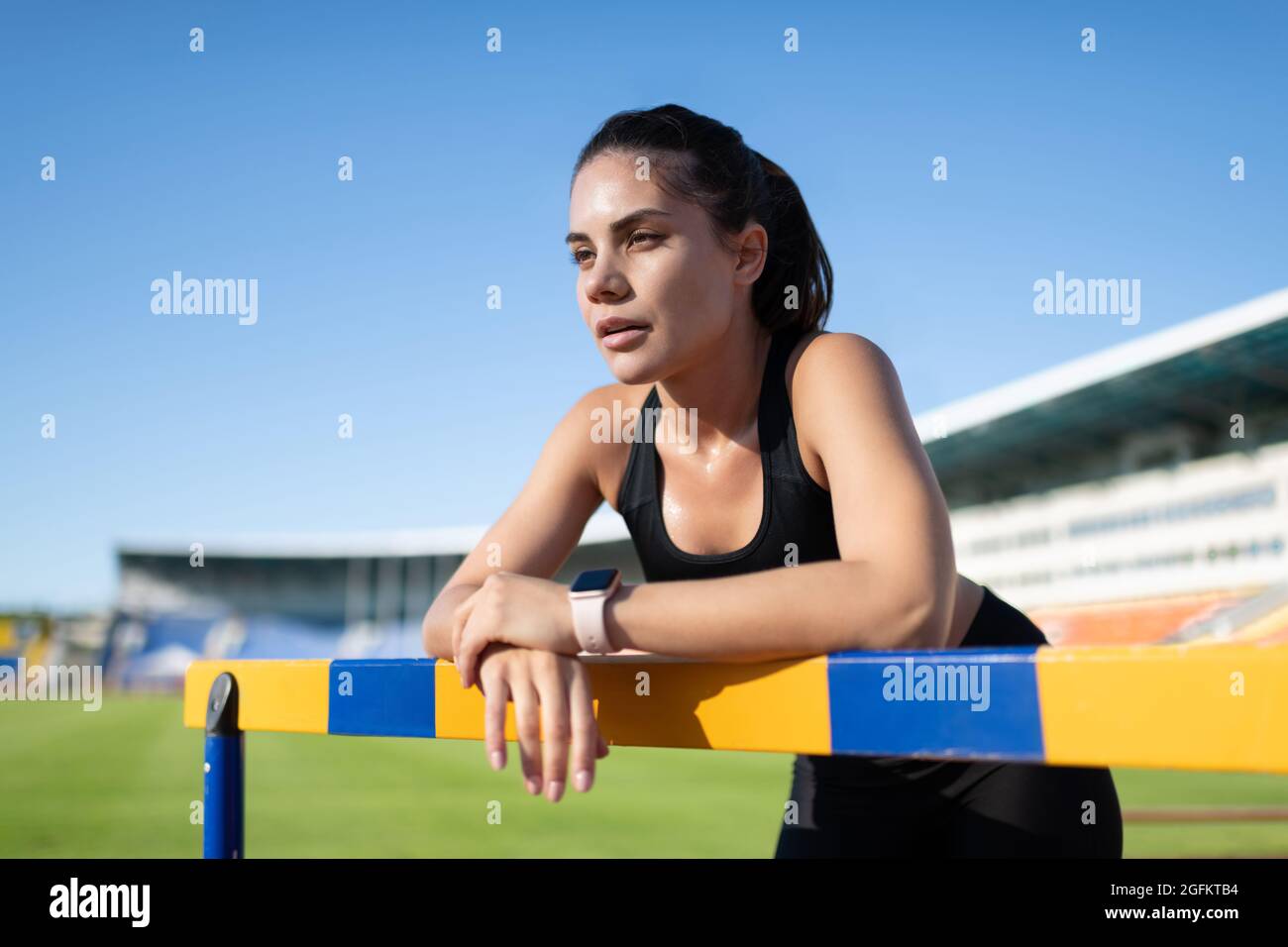Müde, schweißtreibende Sportlerin, die sich an der Barriere lehnt und während der Trainingspause ruht Stockfoto