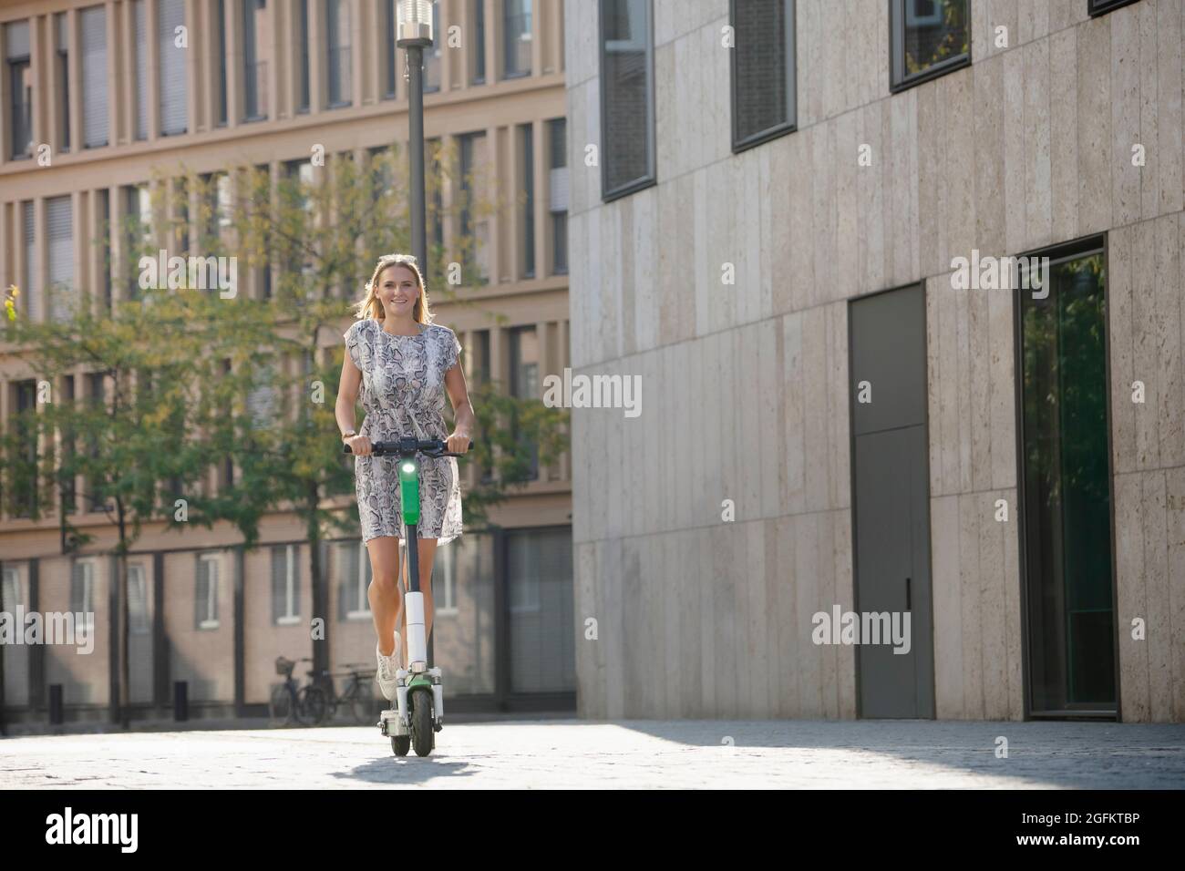 Junge Frau, die im Sommer in der Stadt auf einem E-Scooter reitet Stockfoto