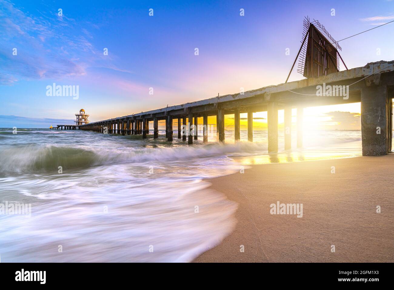 Wunderschöner Sonnenuntergang und sanfte Meereswelle am Strand mit Brückenhafen und Leuchtturm am Ende des Anlegesteg an der Meeresküste für den Transport mit Sonnenuntergang sk Stockfoto